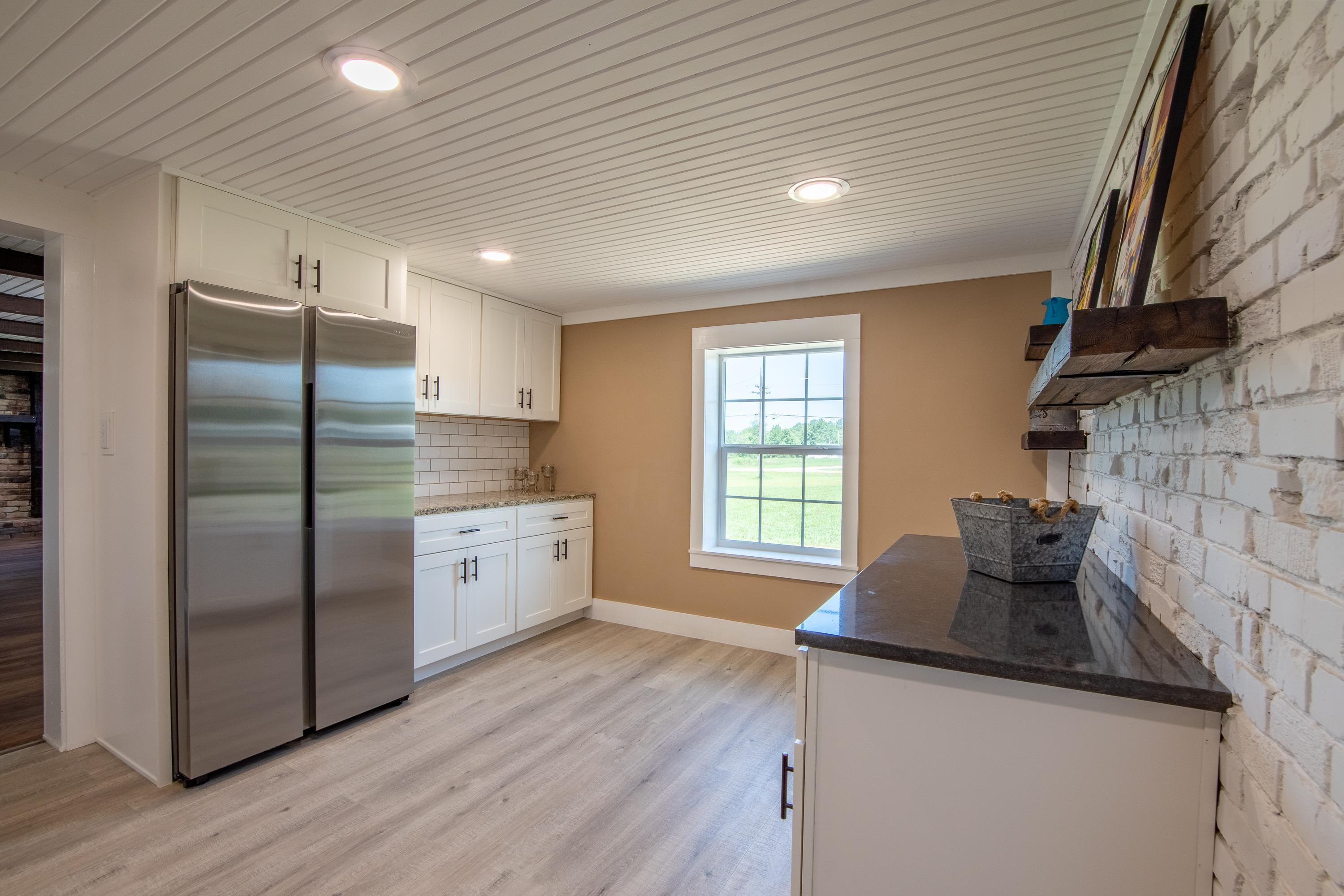 Kitchen with white cabinetry, tasteful backsplash, dark stone counters, light hardwood / wood-style floors, and stainless steel fridge