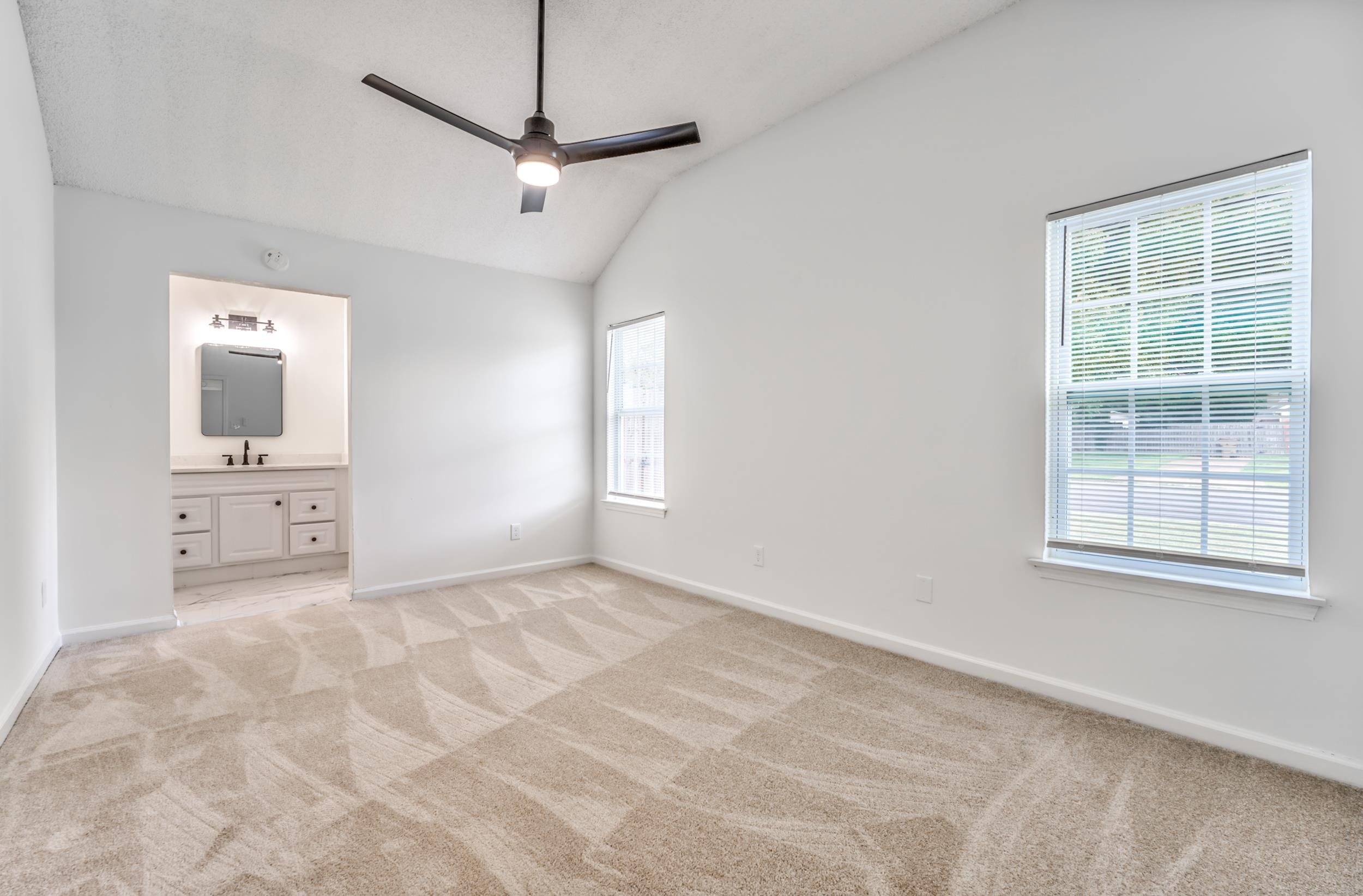 Unfurnished bedroom featuring ensuite bathroom, sink, lofted ceiling, light carpet, and ceiling fan