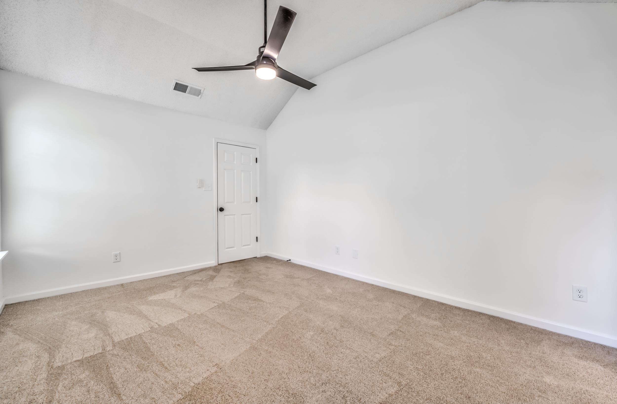 Carpeted empty room with lofted ceiling and ceiling fan