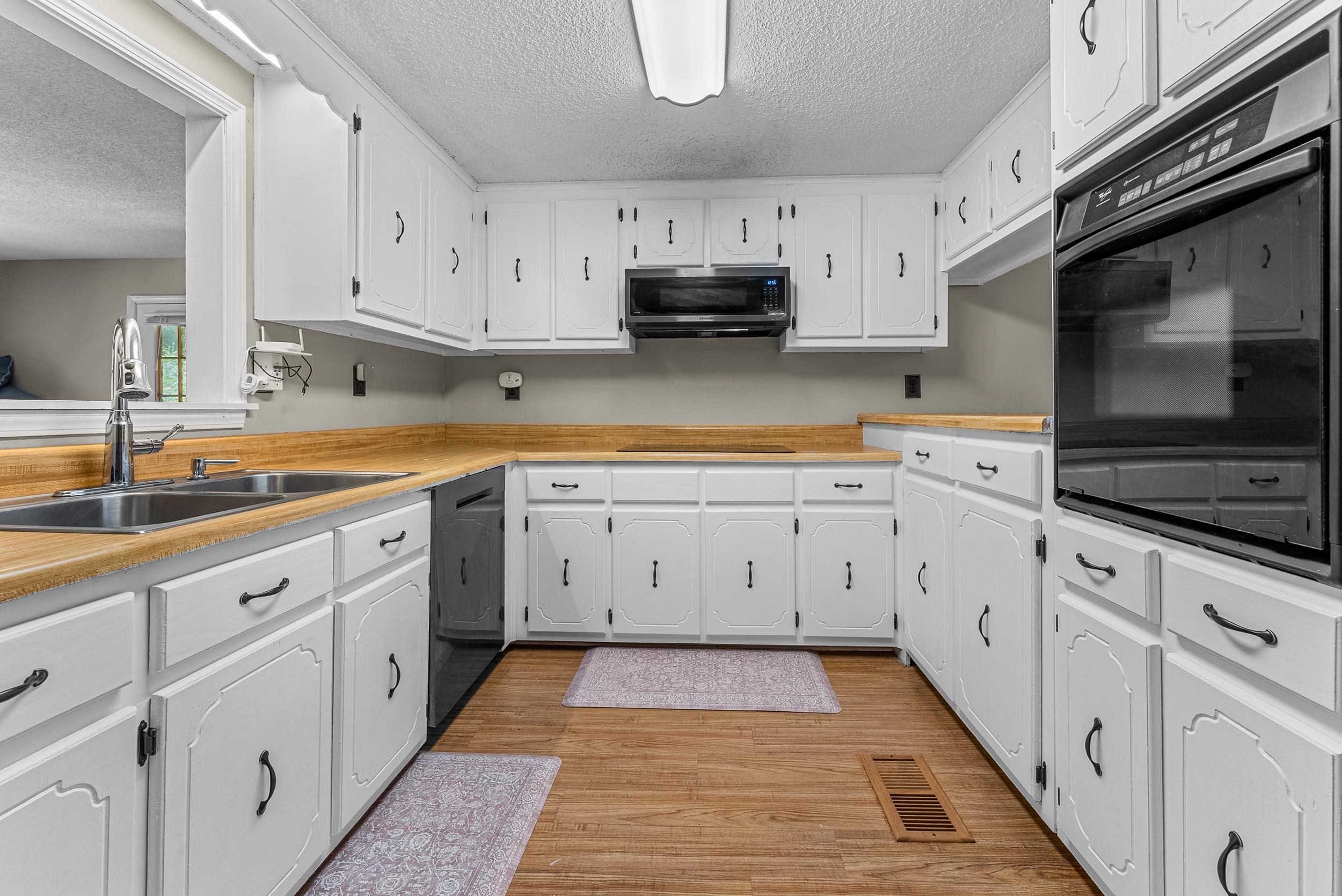 Kitchen with white cabinets, light hardwood / wood-style floors, black appliances, and a textured ceiling