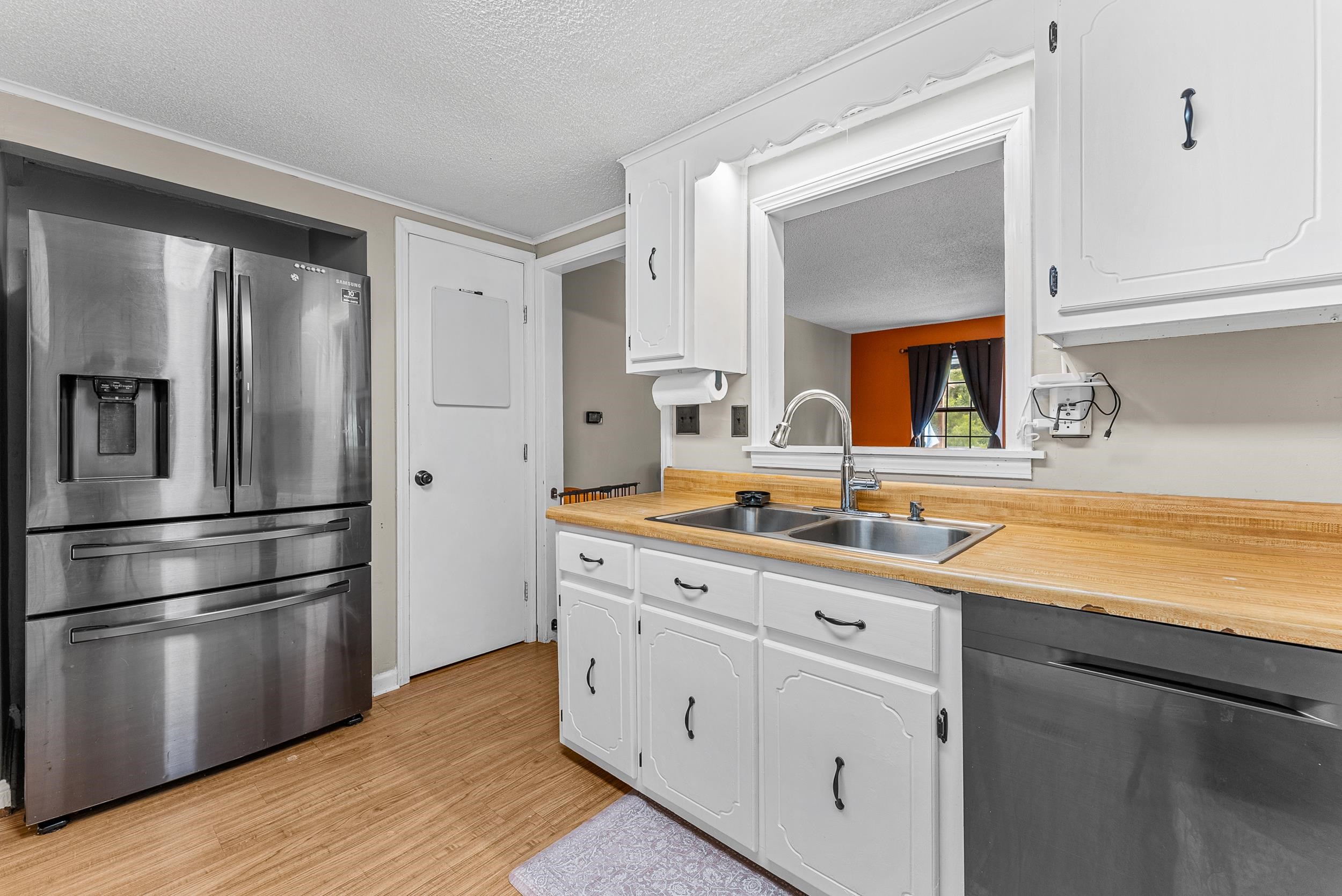 Kitchen featuring white cabinets, stainless steel fridge, sink, dishwashing machine, and light wood-type flooring