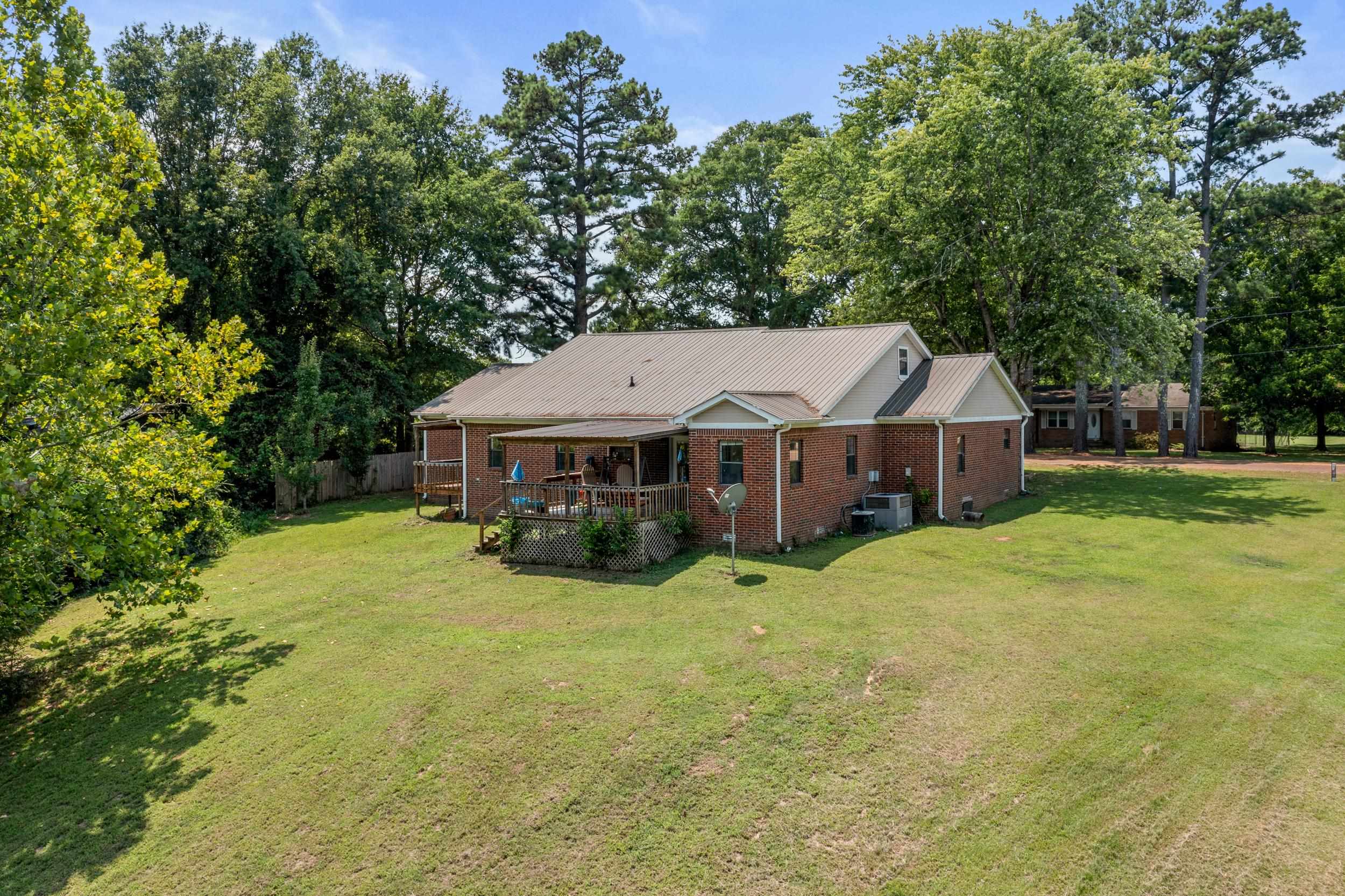 Rear view of house featuring a wooden deck, central AC, and a lawn