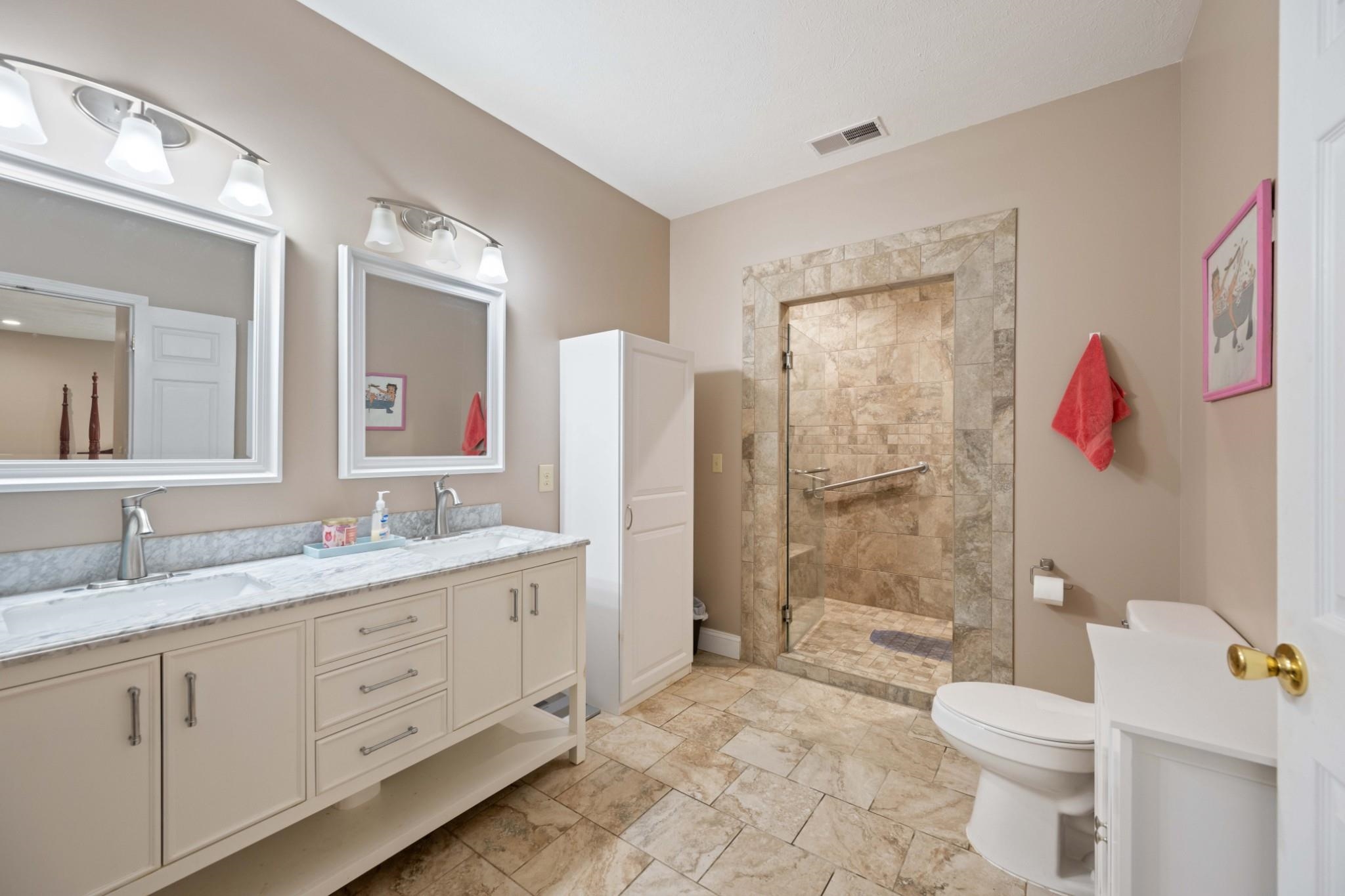 Bathroom featuring tiled shower, double vanity, toilet, and tile patterned floors