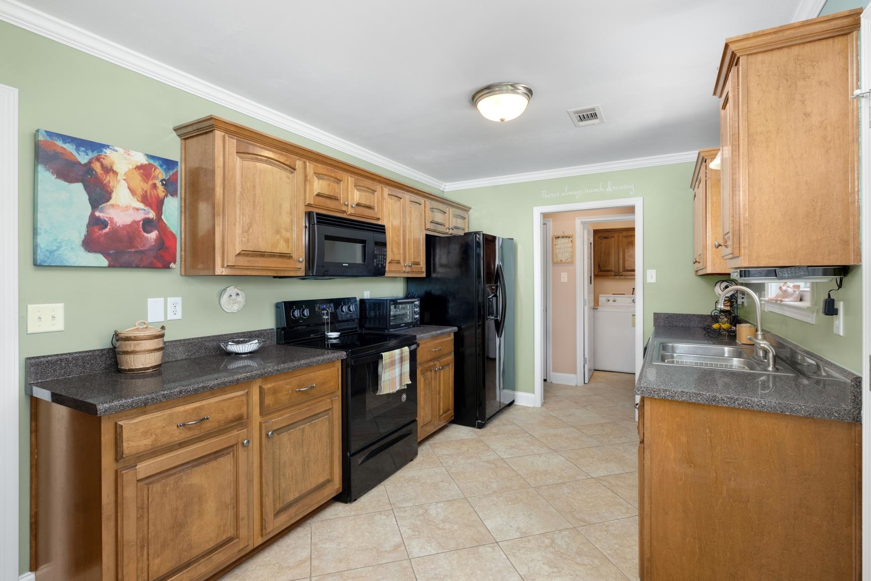 Kitchen with light tile patterned flooring, crown molding, black appliances, and sink