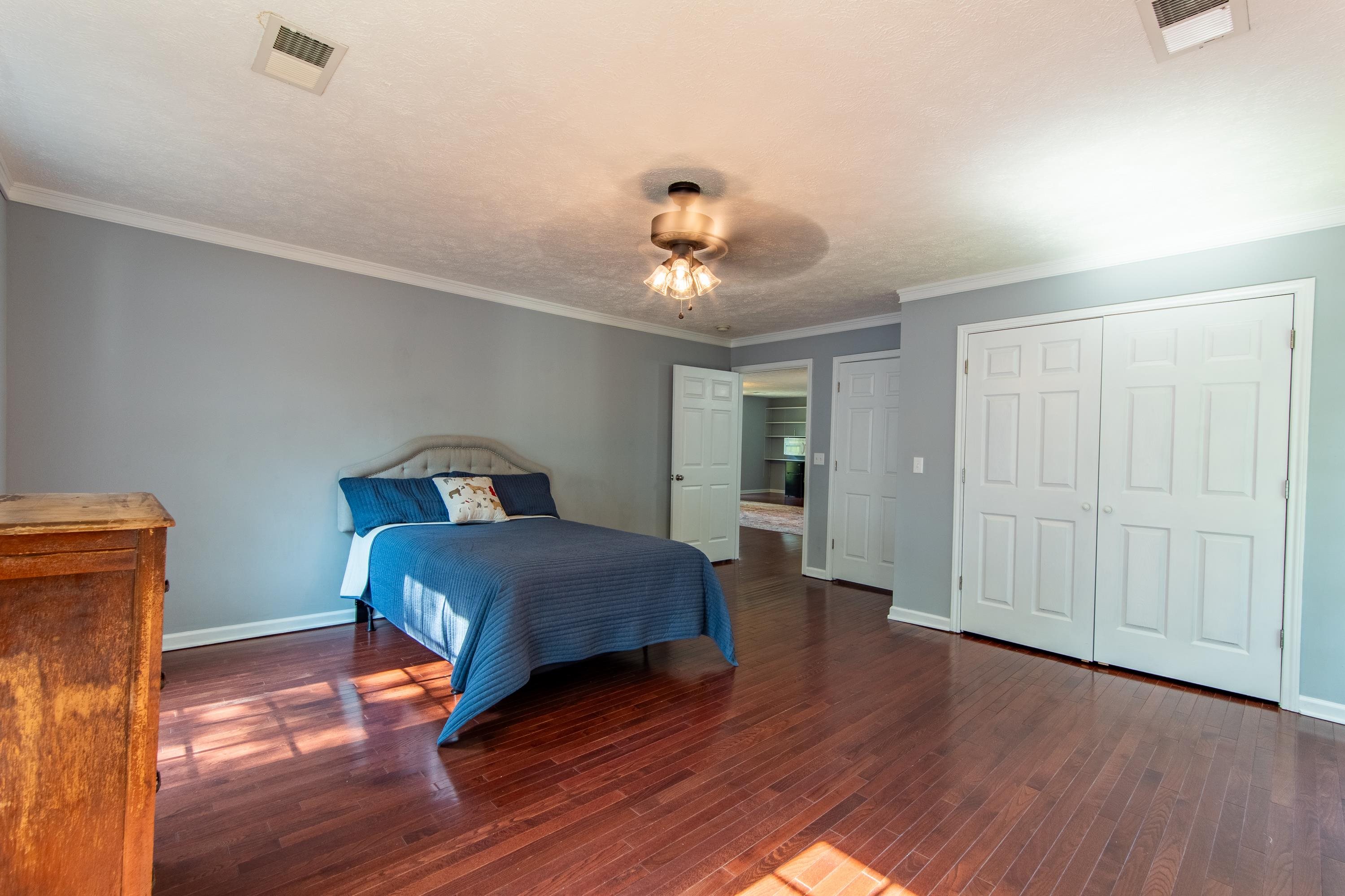 Bedroom with wood-type flooring, crown molding, a closet, and ceiling fan