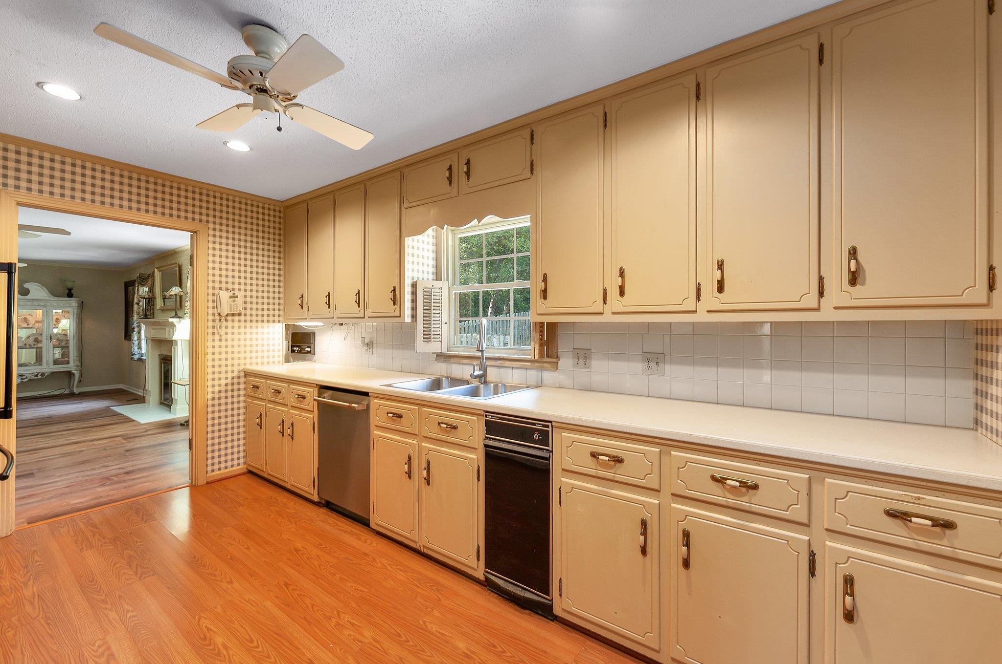 Kitchen featuring sink, backsplash, light hardwood / wood-style floors, stainless steel dishwasher, and ceiling fan