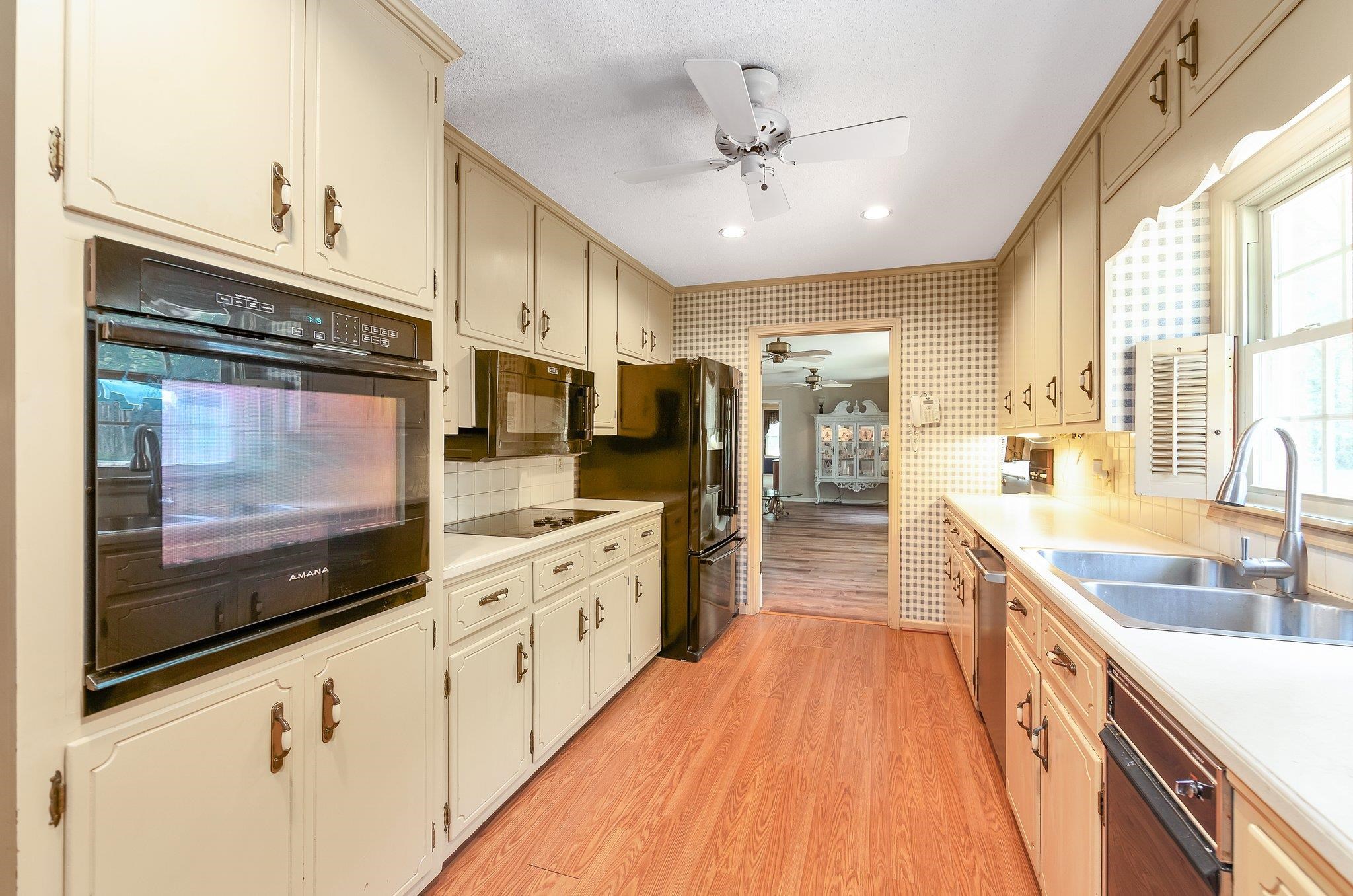Kitchen featuring backsplash, ceiling fan, light hardwood / wood-style floors, black appliances, and sink