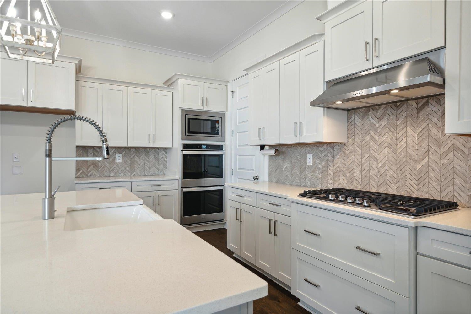 Kitchen featuring white cabinets, stainless steel appliances, decorative backsplash, pendant lighting, and ornamental molding