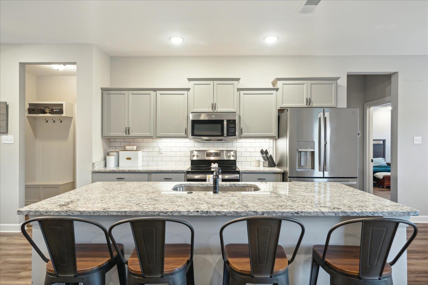 Kitchen with appliances with stainless steel finishes, dark hardwood / wood-style floors, decorative backsplash, and a center island with sink