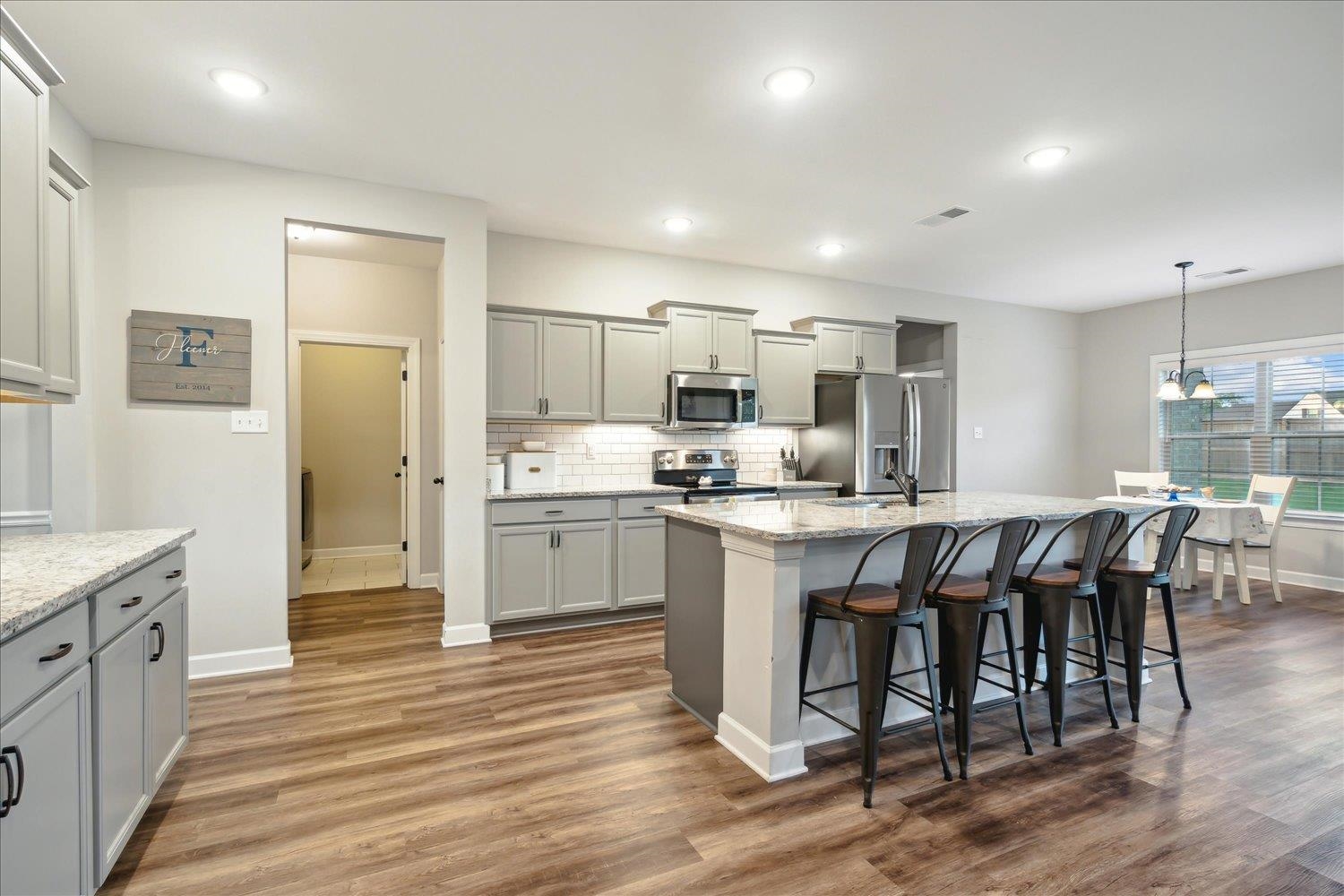 Kitchen featuring wood-type flooring, tasteful backsplash, an island with sink, and stainless steel appliances