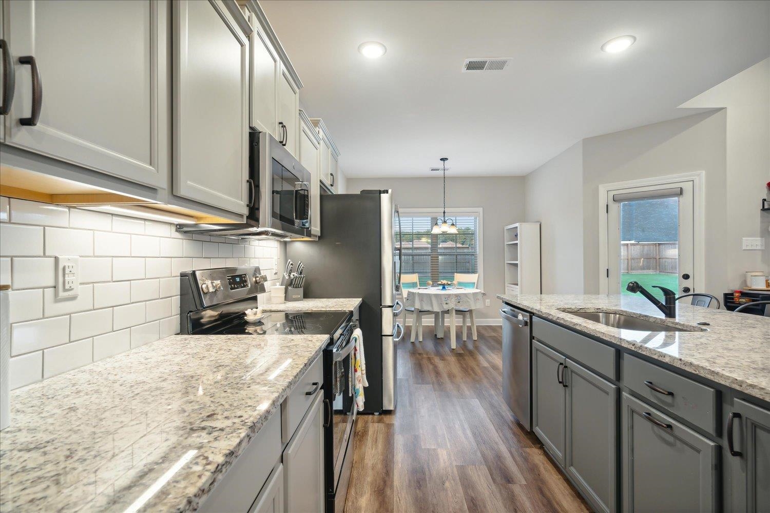 Kitchen featuring dark hardwood / wood-style floors, light stone countertops, appliances with stainless steel finishes, decorative backsplash, and sink