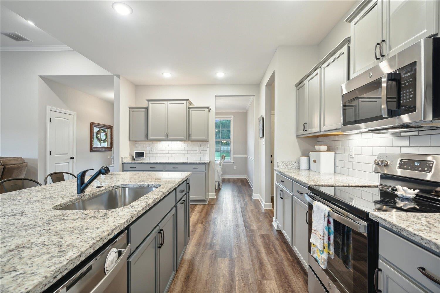 Kitchen with dark wood-type flooring, stainless steel appliances, light stone countertops, decorative backsplash, and sink