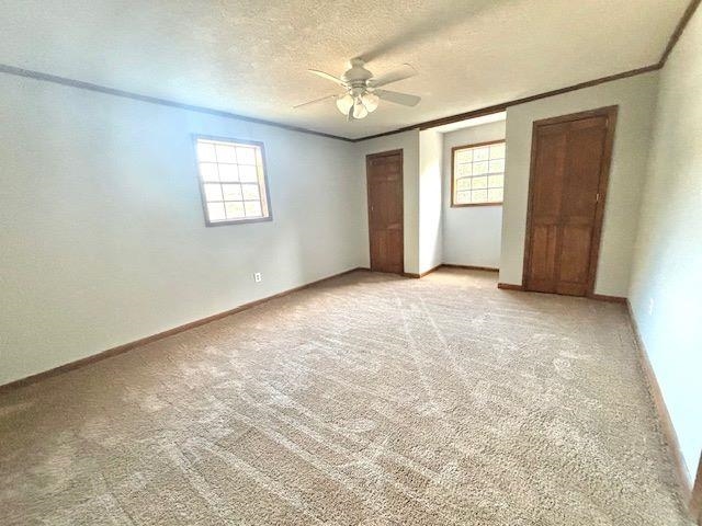 Unfurnished bedroom featuring multiple windows, light carpet, ceiling fan, and a textured ceiling