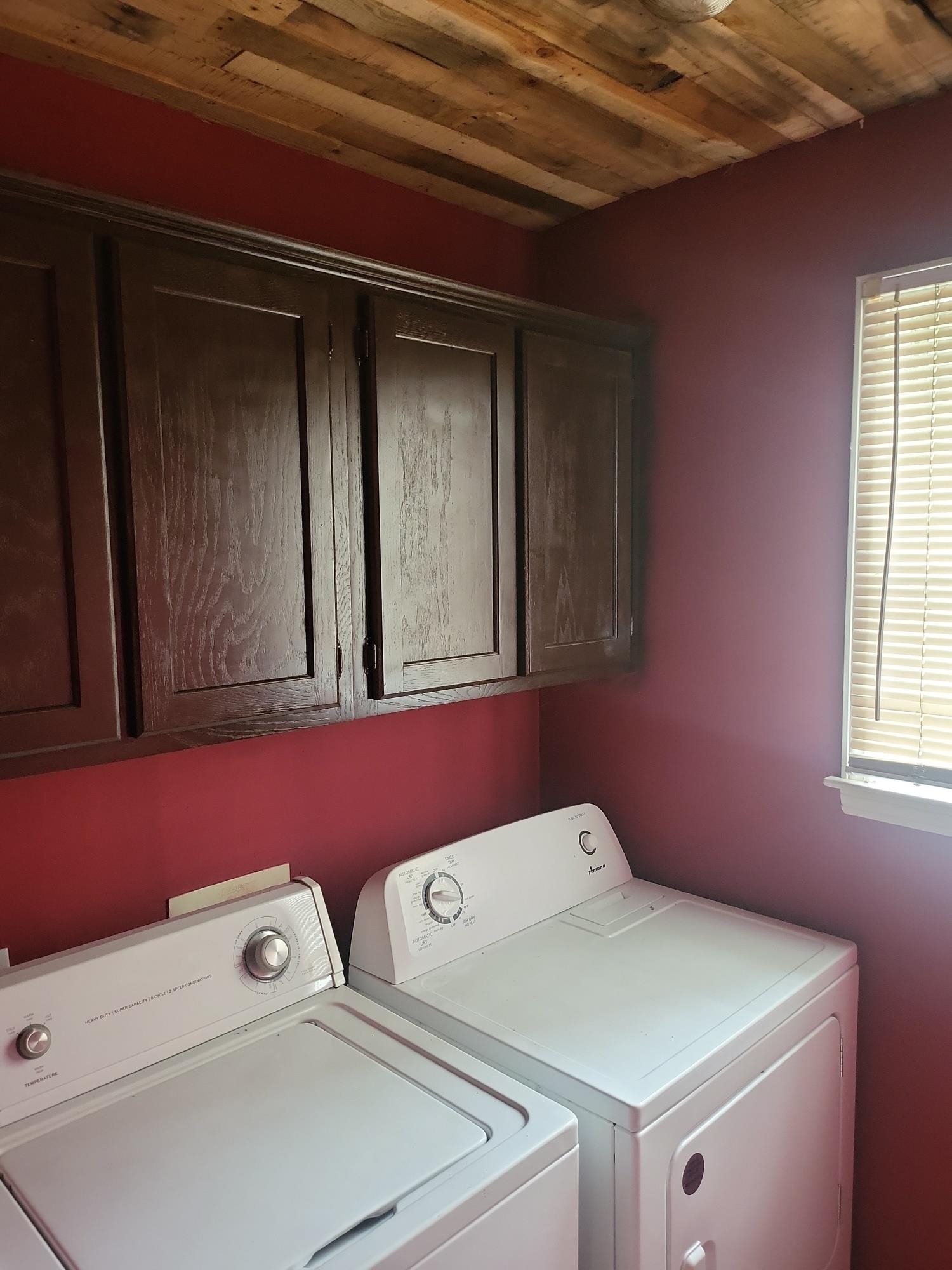 Clothes washing area with wood ceiling, washer and clothes dryer, and cabinets