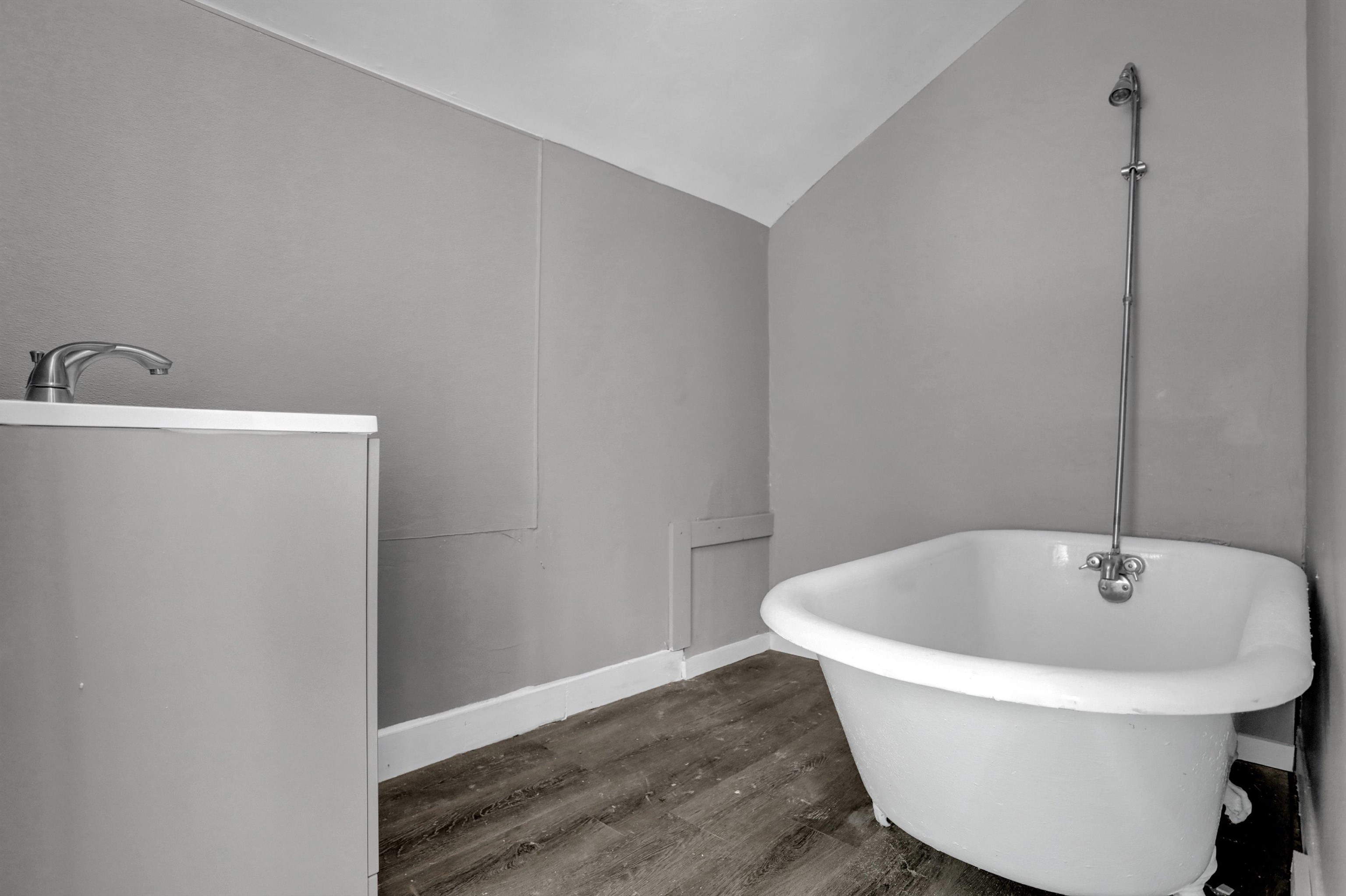 Bathroom with hardwood / wood-style flooring, a tub to relax in, and vaulted ceiling