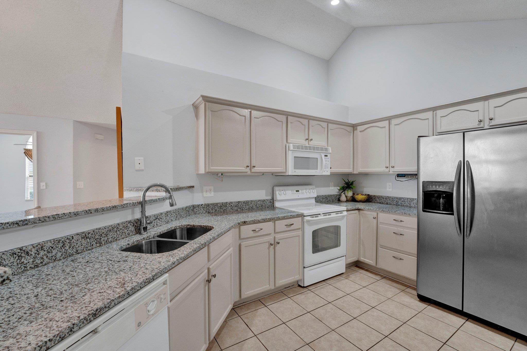 Kitchen with white appliances, light stone countertops, high vaulted ceiling, sink, and light tile patterned flooring