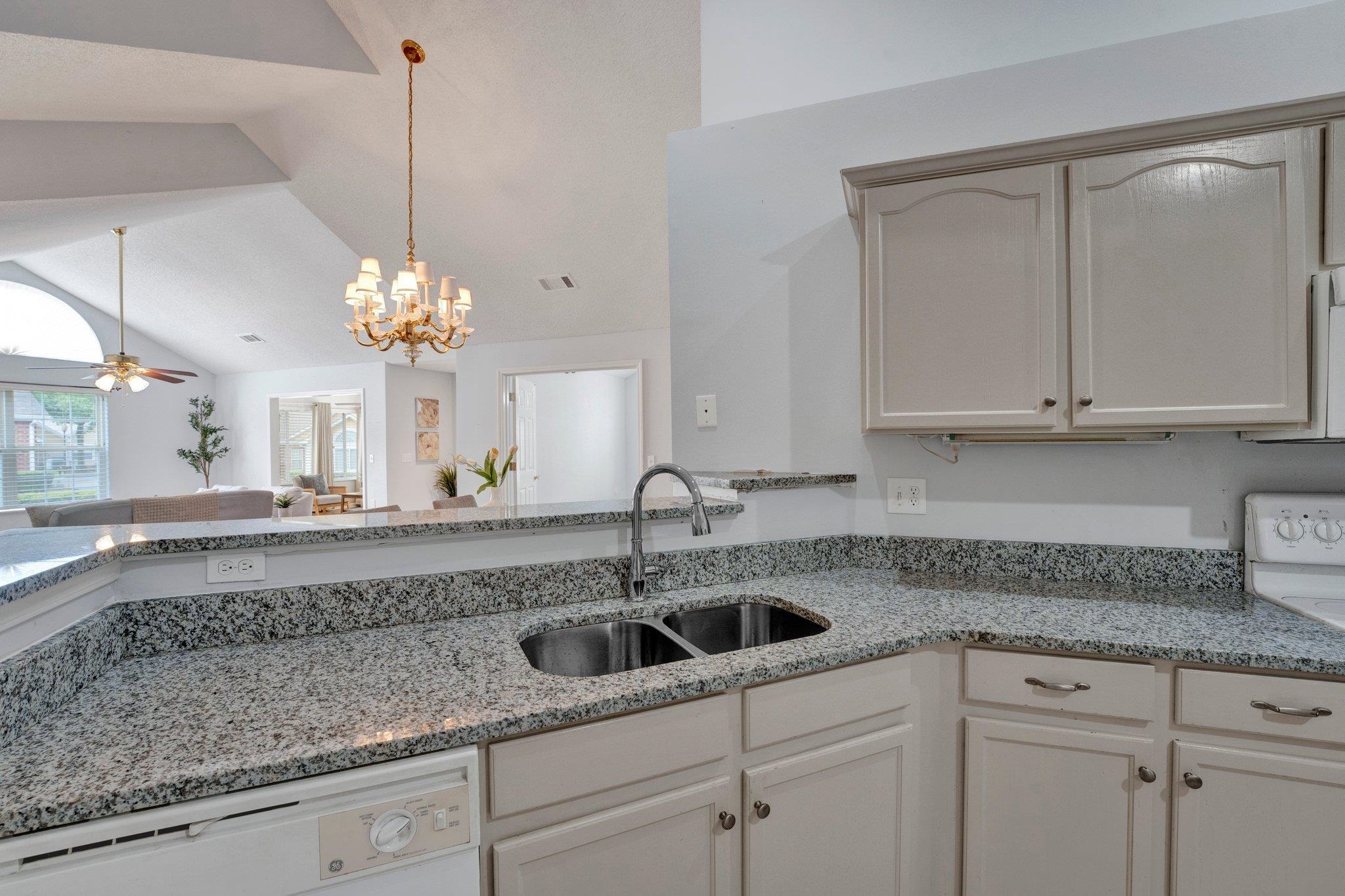 Kitchen with ceiling fan with notable chandelier, white dishwasher, light stone counters, lofted ceiling, and sink