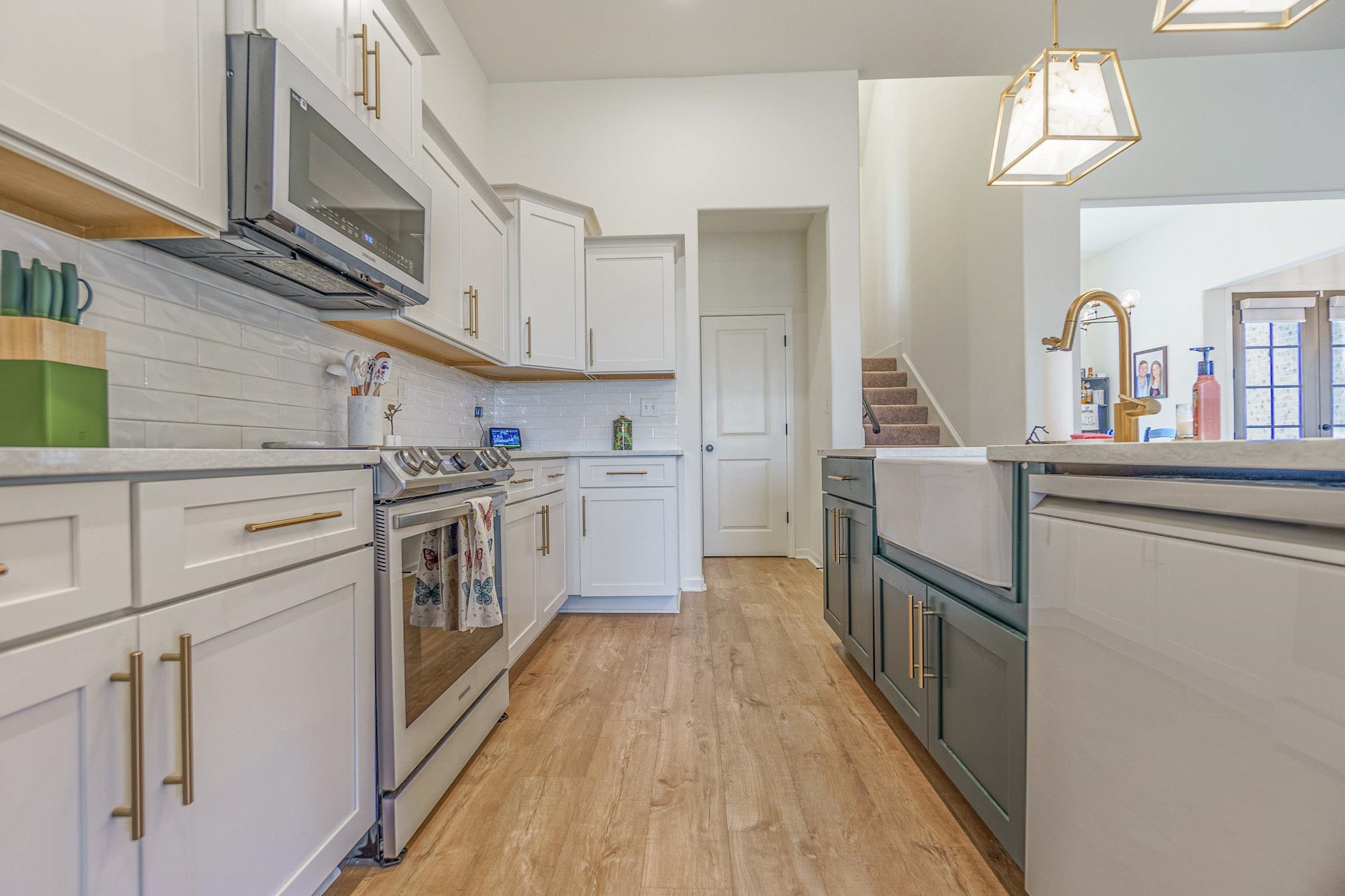 Kitchen with appliances with stainless steel finishes, white cabinets, backsplash, light hardwood / wood-style floors, and decorative light fixtures