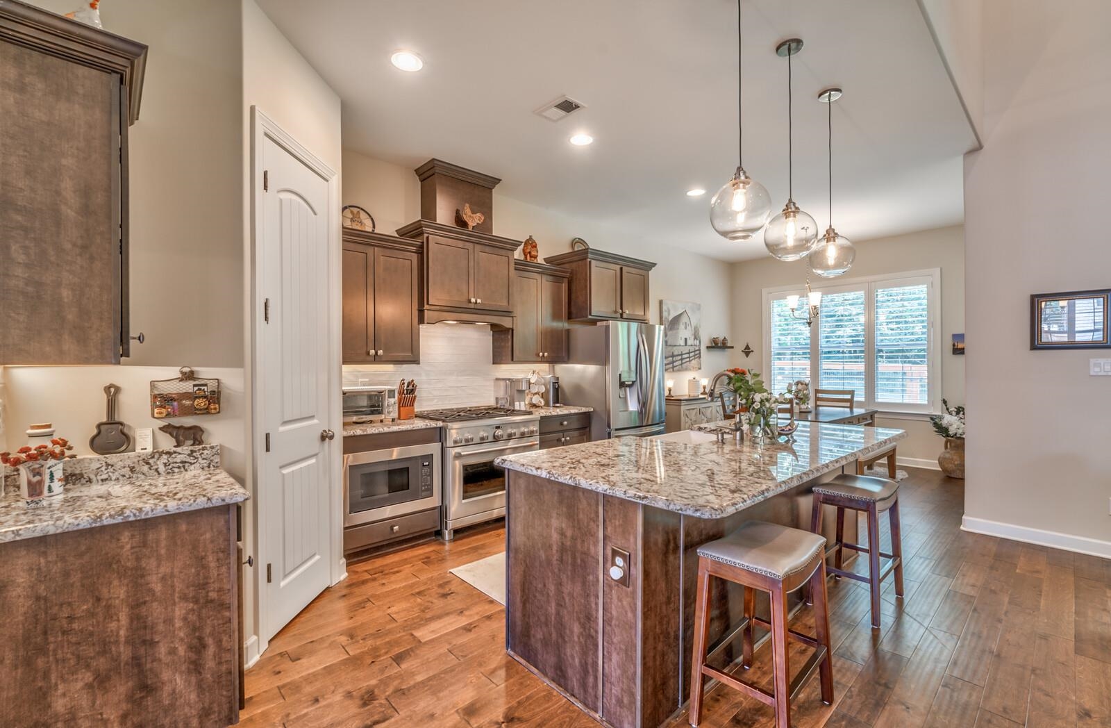 Kitchen featuring light stone counters, stainless steel appliances, hanging light fixtures, hardwood / wood-style flooring, and a kitchen bar