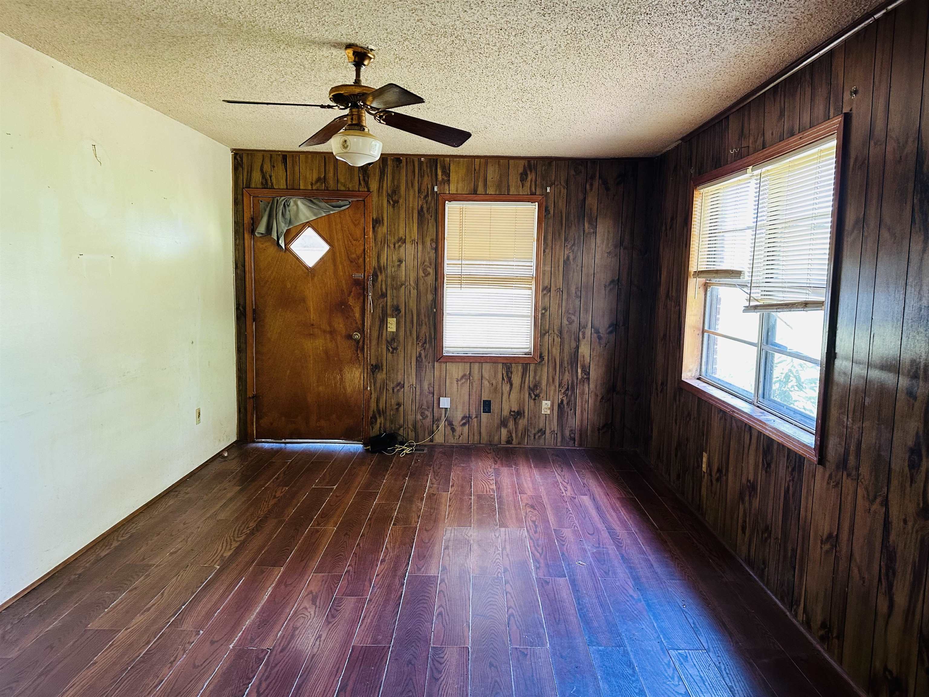 Unfurnished room with ceiling fan, a textured ceiling, wooden walls, and hardwood / wood-style flooring