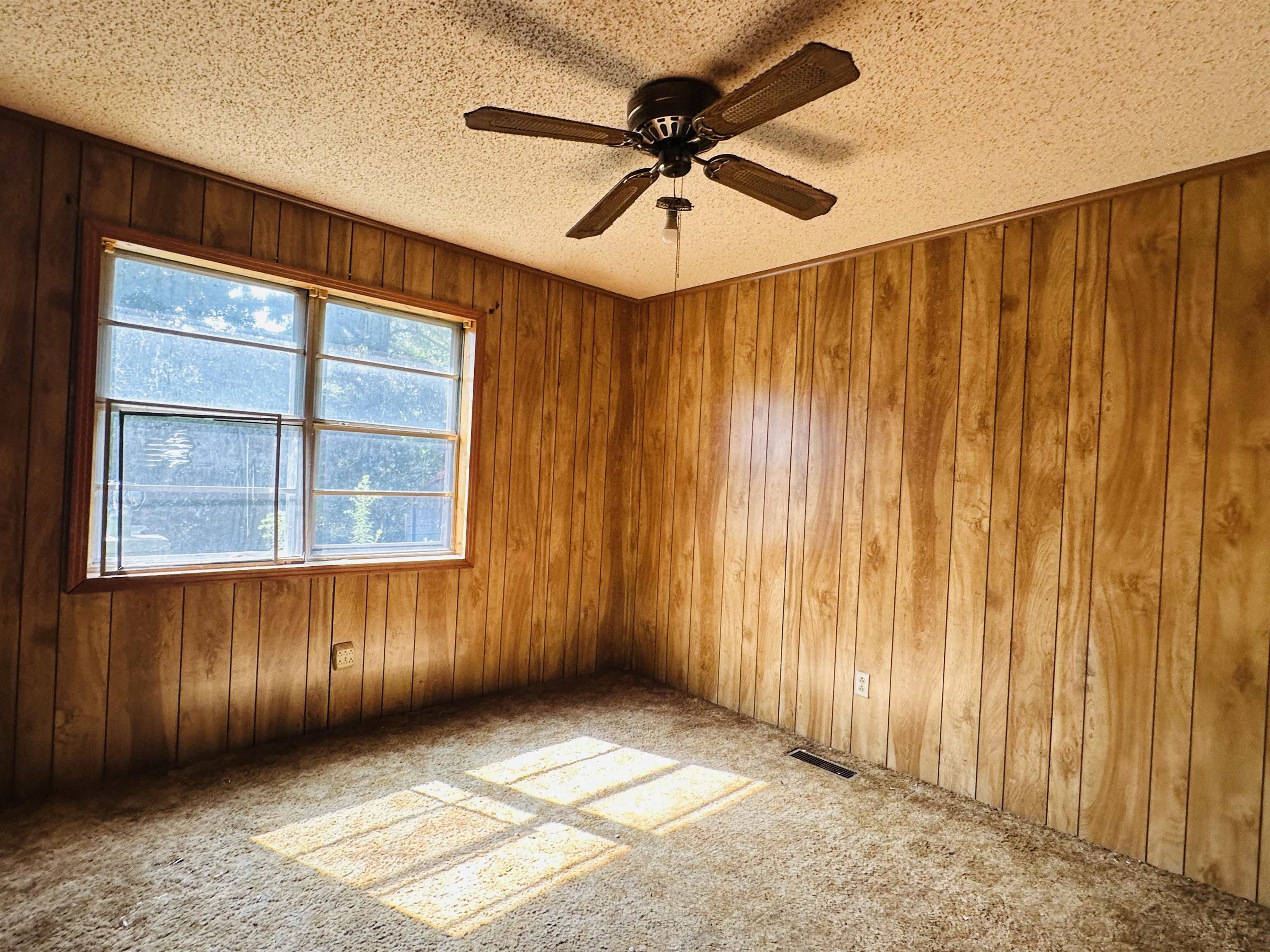 Carpeted empty room with wood walls, a textured ceiling, and ceiling fan