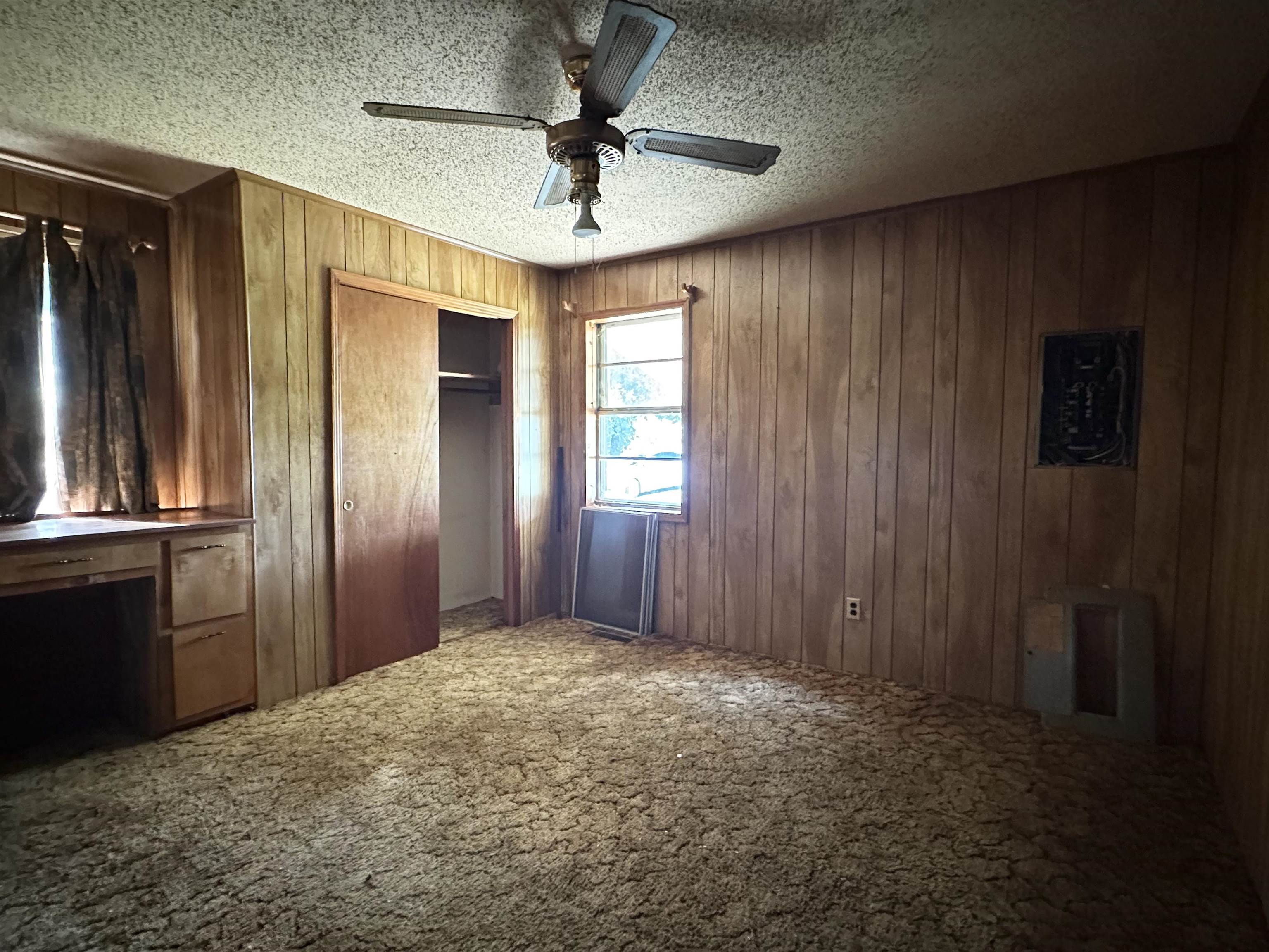 Unfurnished bedroom with ceiling fan, carpet flooring, a textured ceiling, and wooden walls