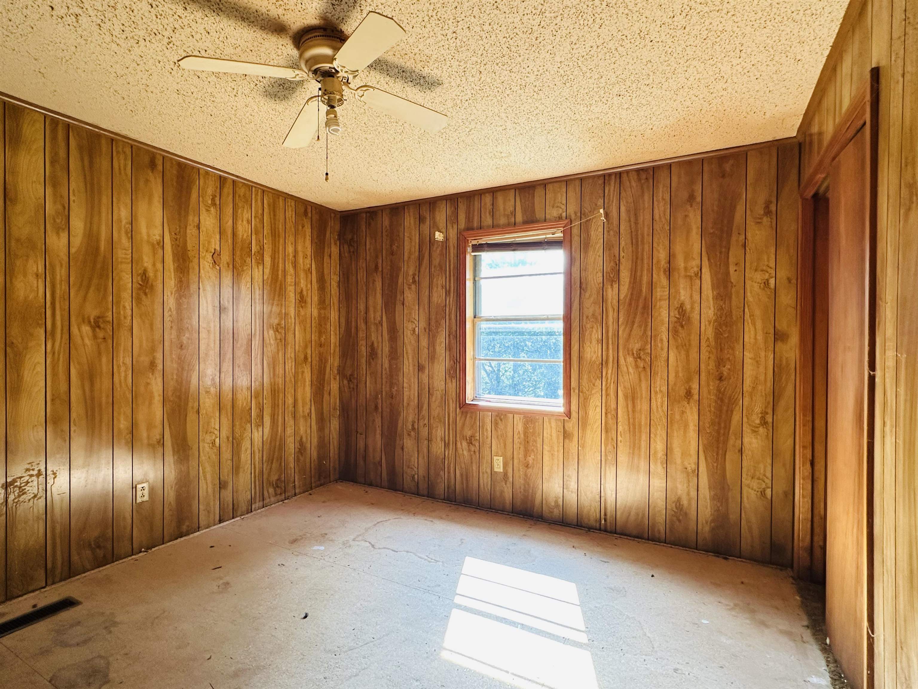 Unfurnished room featuring wood walls, a textured ceiling, and ceiling fan