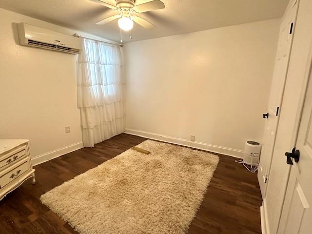 Unfurnished bedroom with ceiling fan, a wall mounted AC, and dark hardwood / wood-style floors