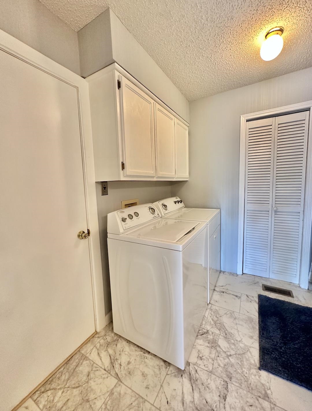 Laundry area featuring a textured ceiling, light tile patterned flooring, separate washer and dryer, and cabinets