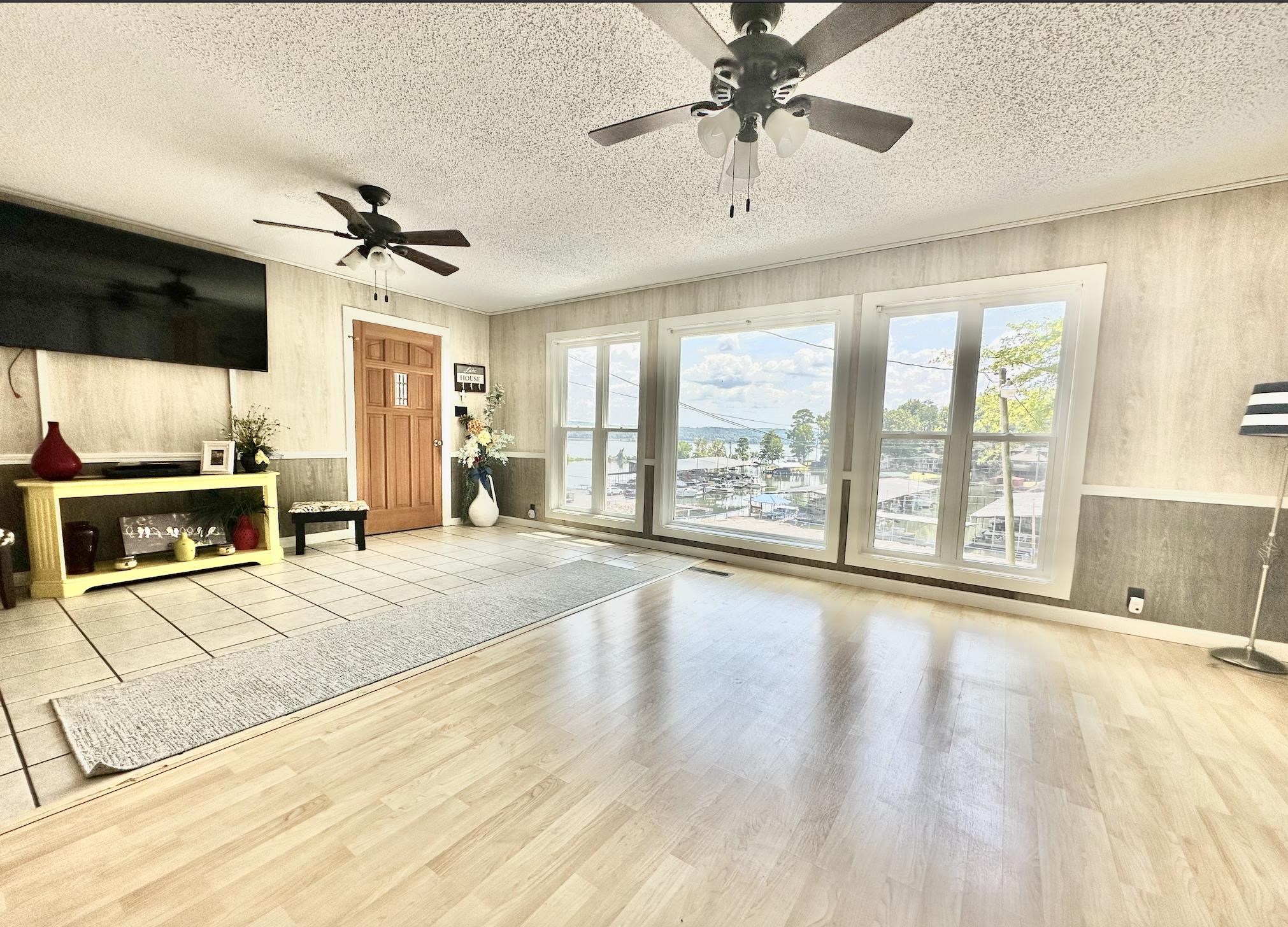 Living room with a textured ceiling, wooden walls, ceiling fan, and light wood-type flooring