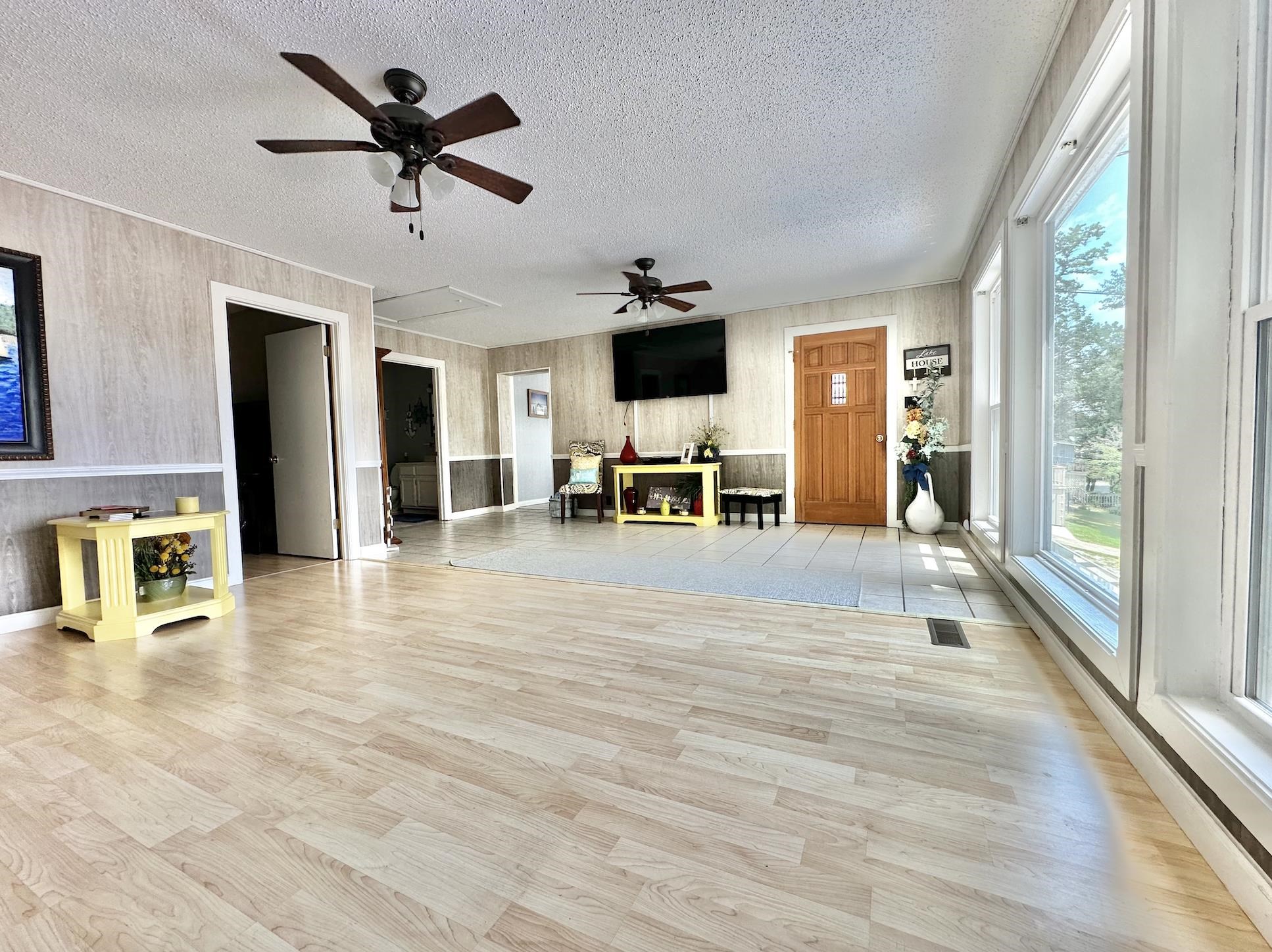 Unfurnished living room with a textured ceiling, wooden walls, ceiling fan, and light hardwood / wood-style floors