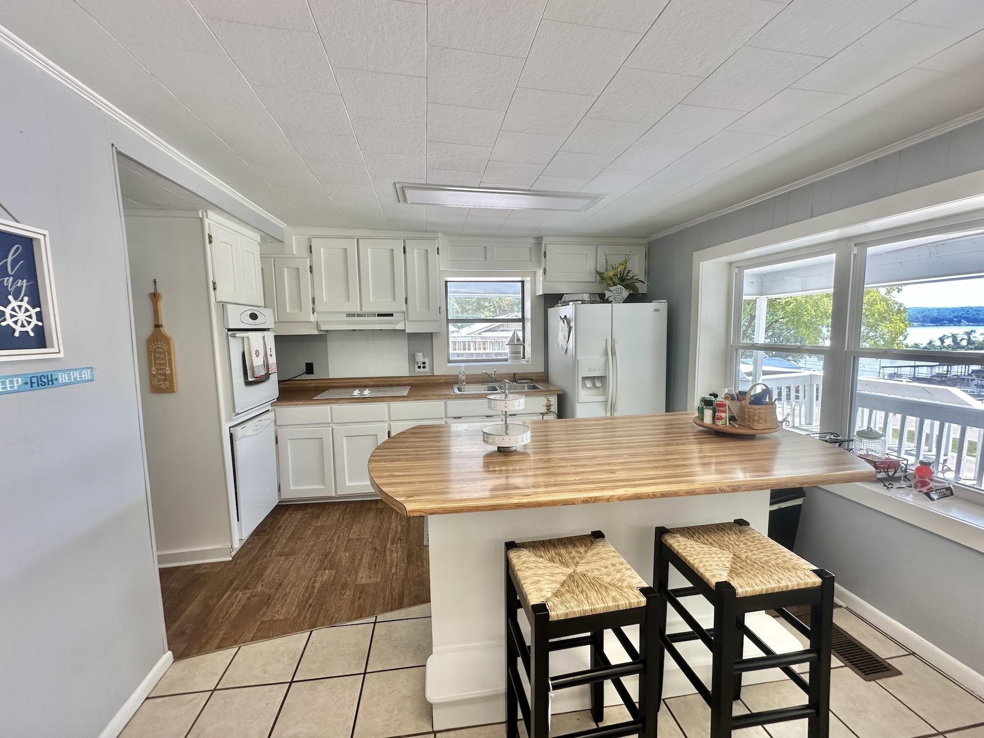 Kitchen featuring light hardwood / wood-style flooring, ornamental molding, white cabinets, white fridge with ice dispenser, and a breakfast bar area