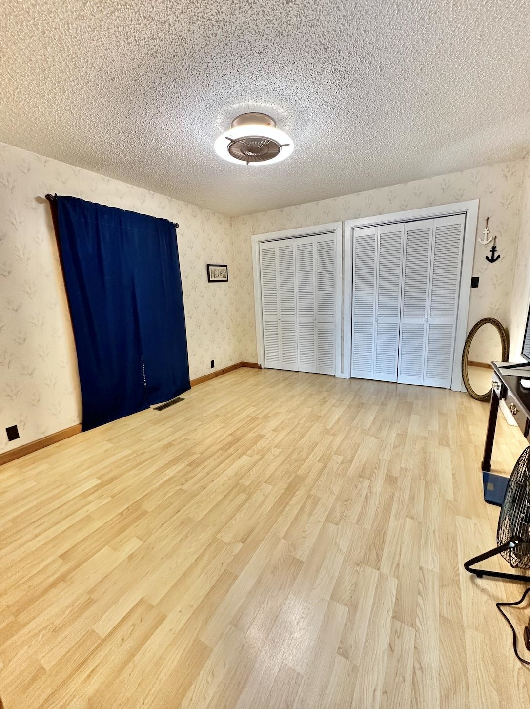 Unfurnished bedroom with a textured ceiling, light hardwood / wood-style flooring, and two closets