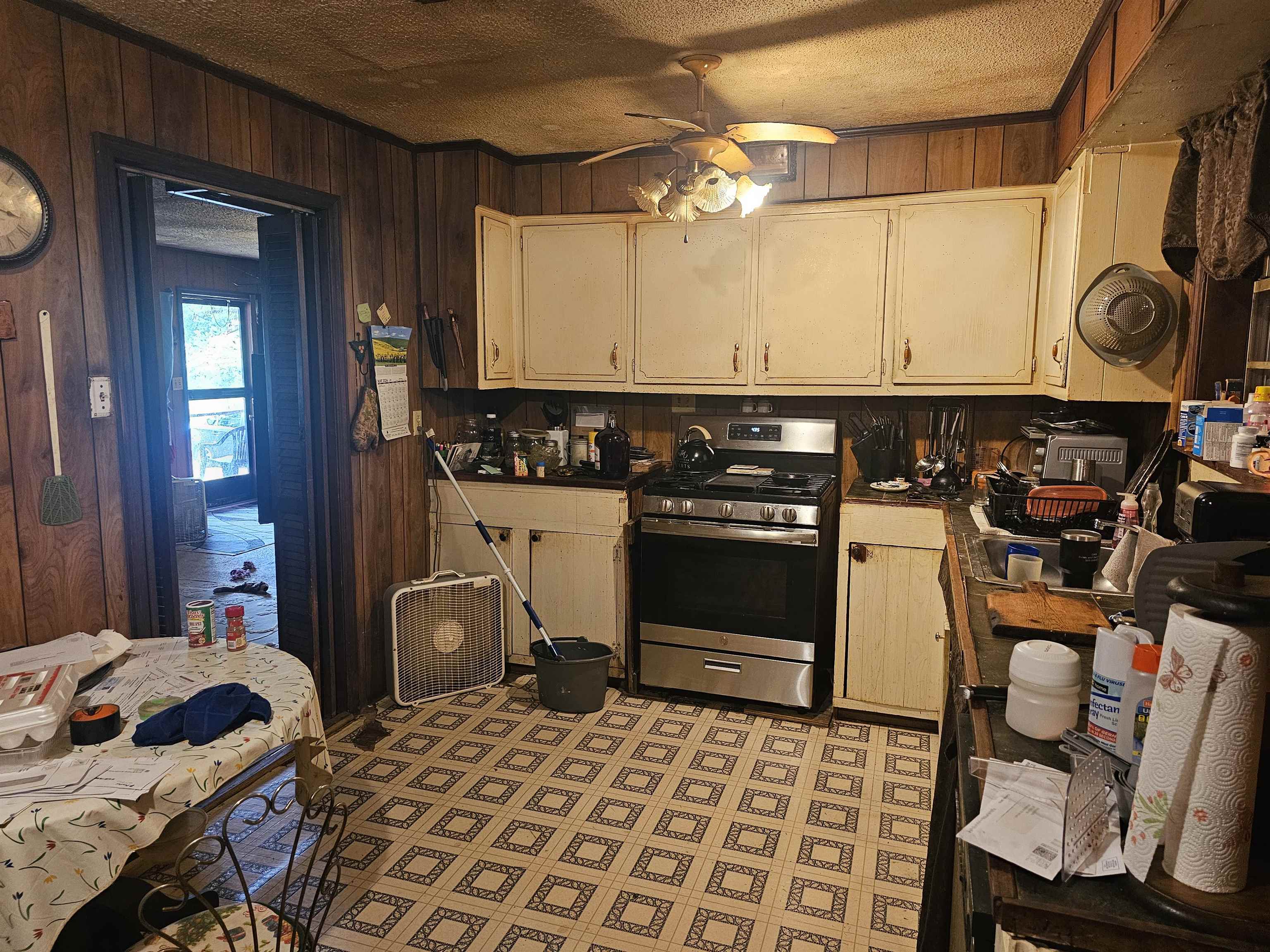 Kitchen featuring ceiling fan, wooden walls, tile patterned flooring, stainless steel range with gas cooktop, and a textured ceiling