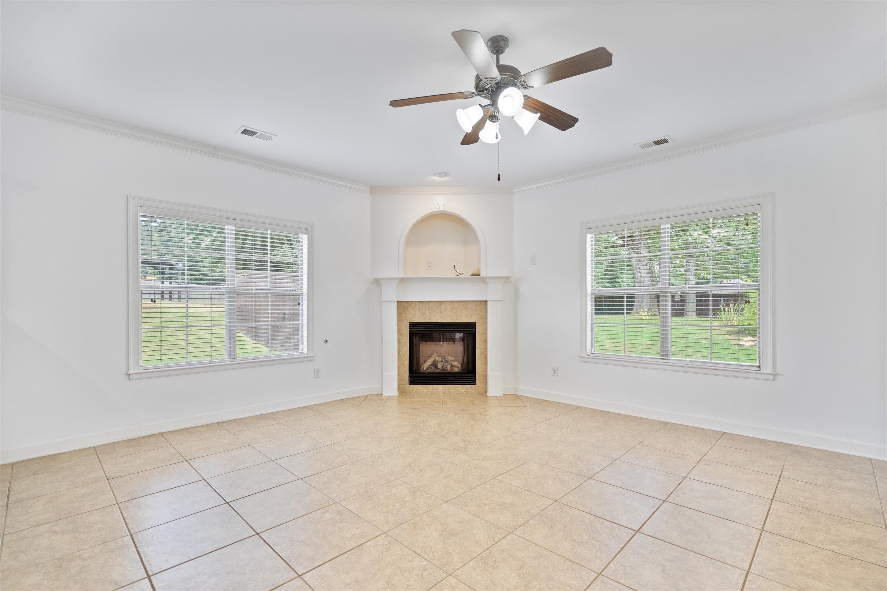 Unfurnished living room featuring ceiling fan, ornamental molding, a tile fireplace, and light tile patterned floors