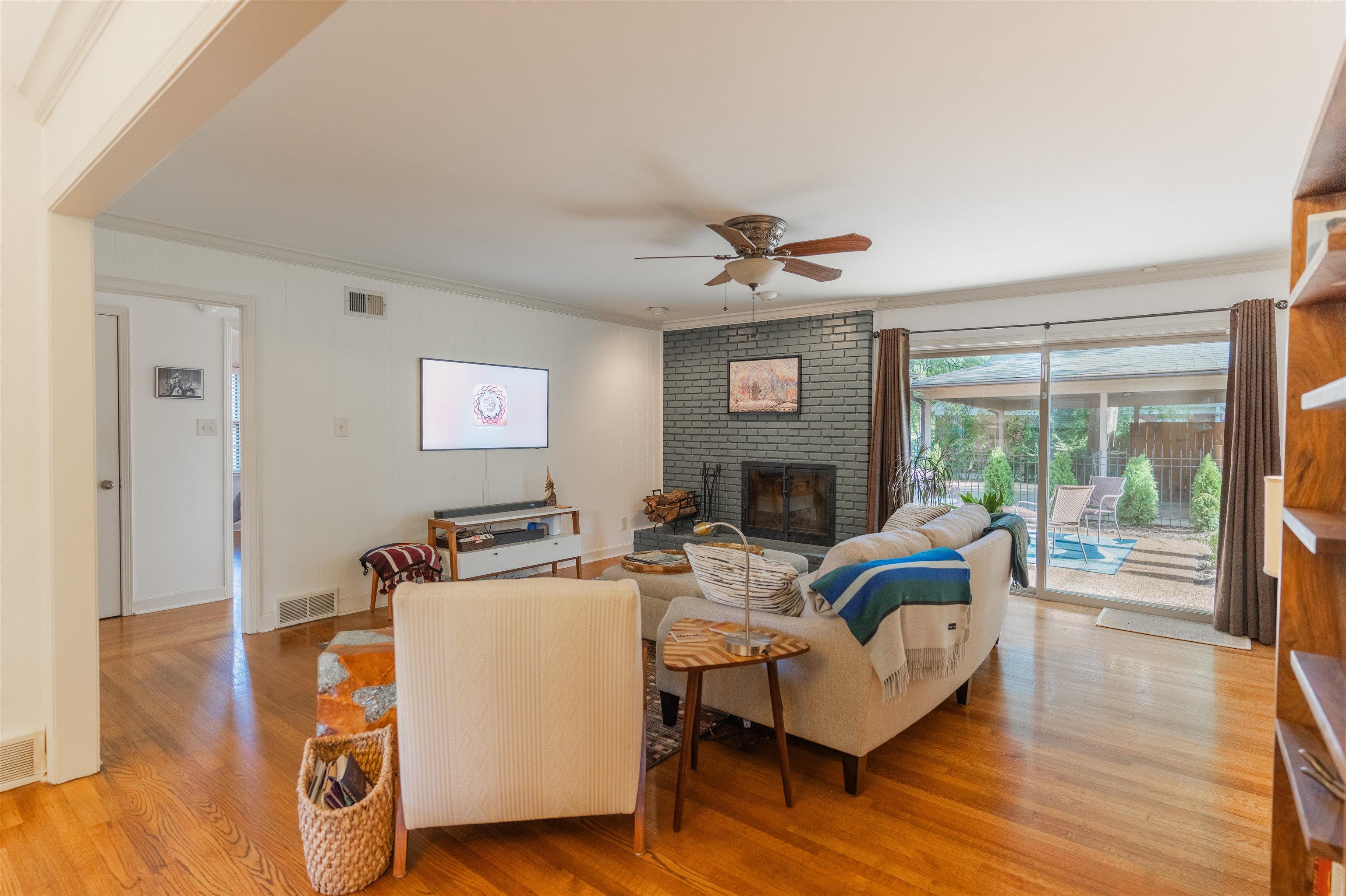 Living room featuring light hardwood / wood-style flooring, brick wall, crown molding, a fireplace, and ceiling fan