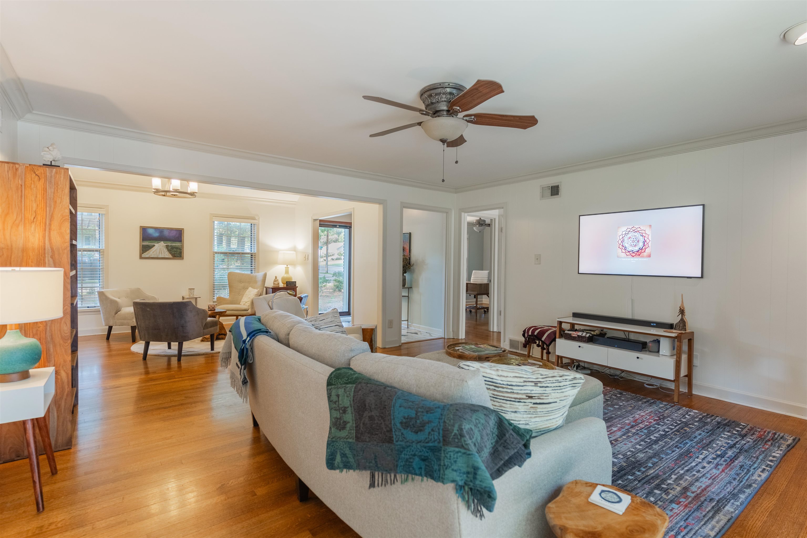 Living room featuring light hardwood / wood-style flooring, crown molding, and ceiling fan with notable chandelier