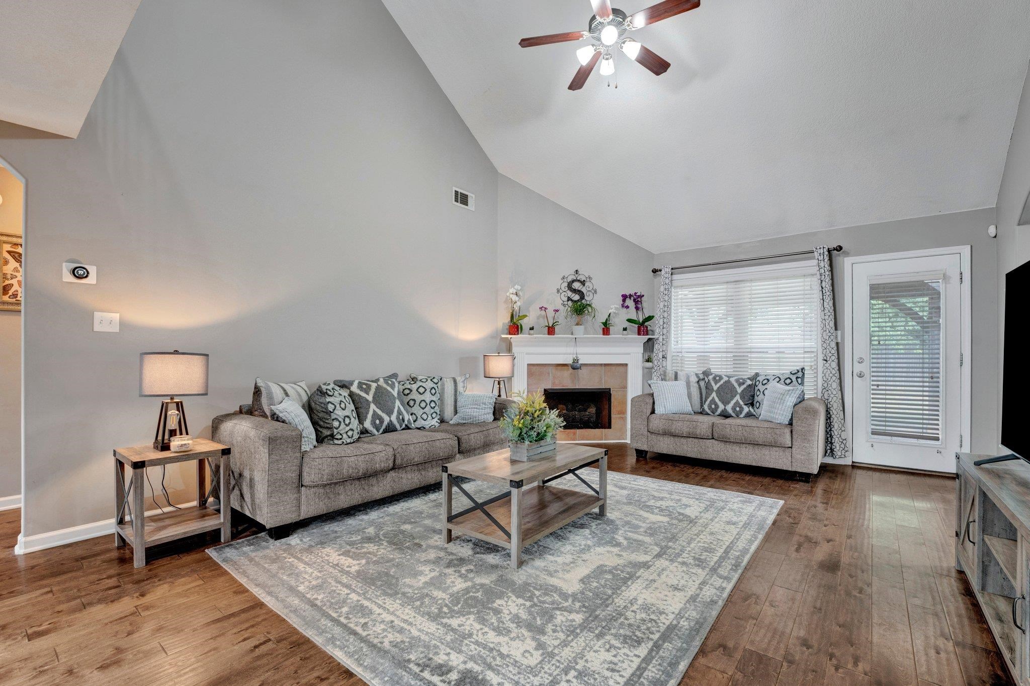 Living room featuring hardwood / wood-style flooring, high vaulted ceiling, a tile fireplace, and ceiling fan