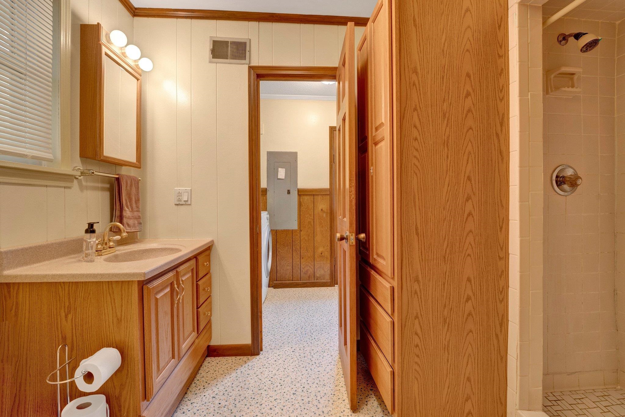 Bathroom featuring a tile shower, vanity, washer / dryer, ornamental molding, and electric panel