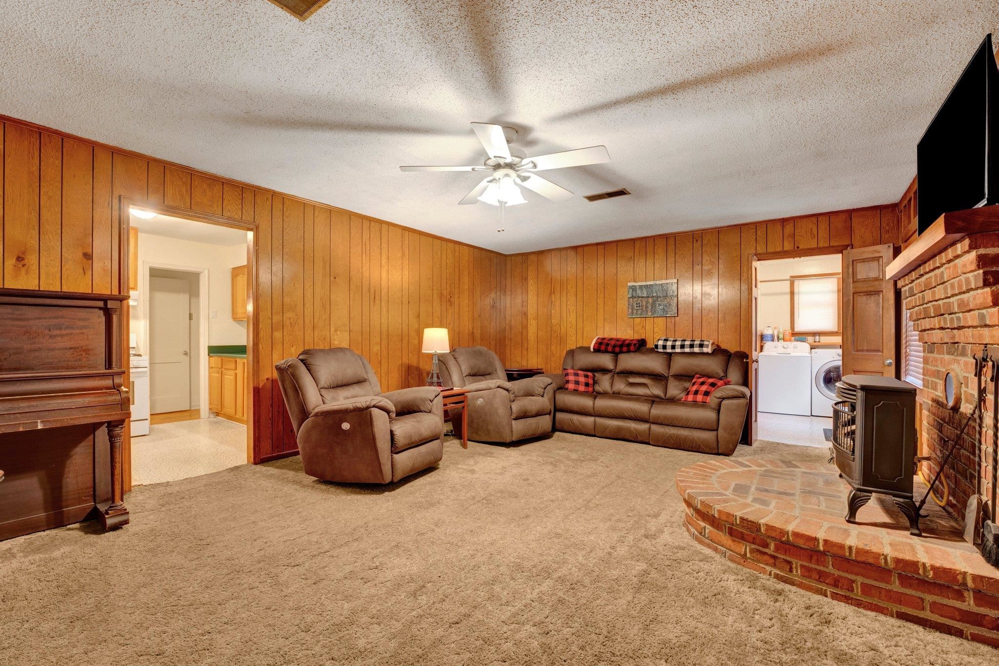 Living room featuring wood walls, ceiling fan, a wood stove, and light carpet