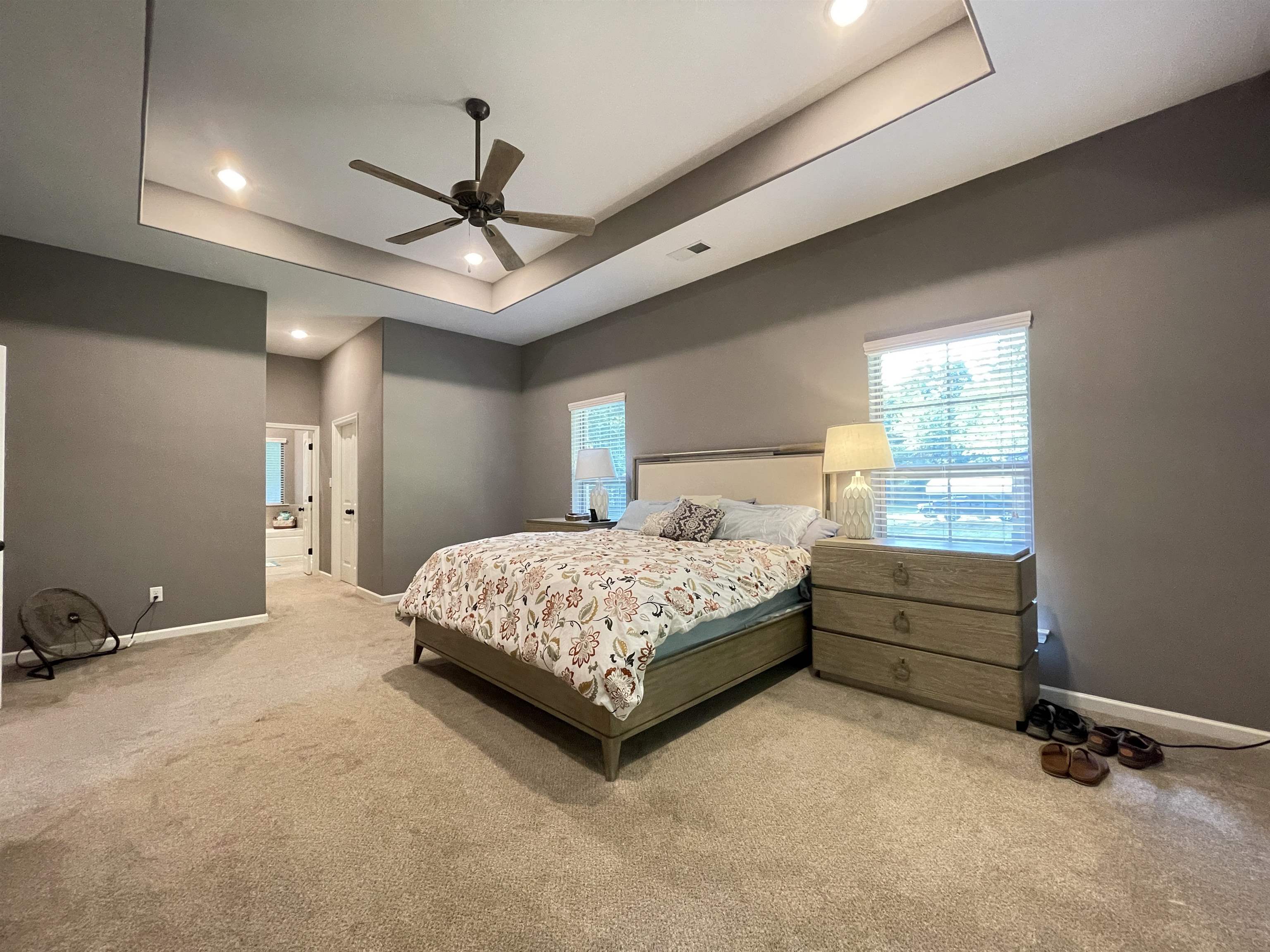 Carpeted bedroom with ceiling fan, ensuite bathroom, and a tray ceiling