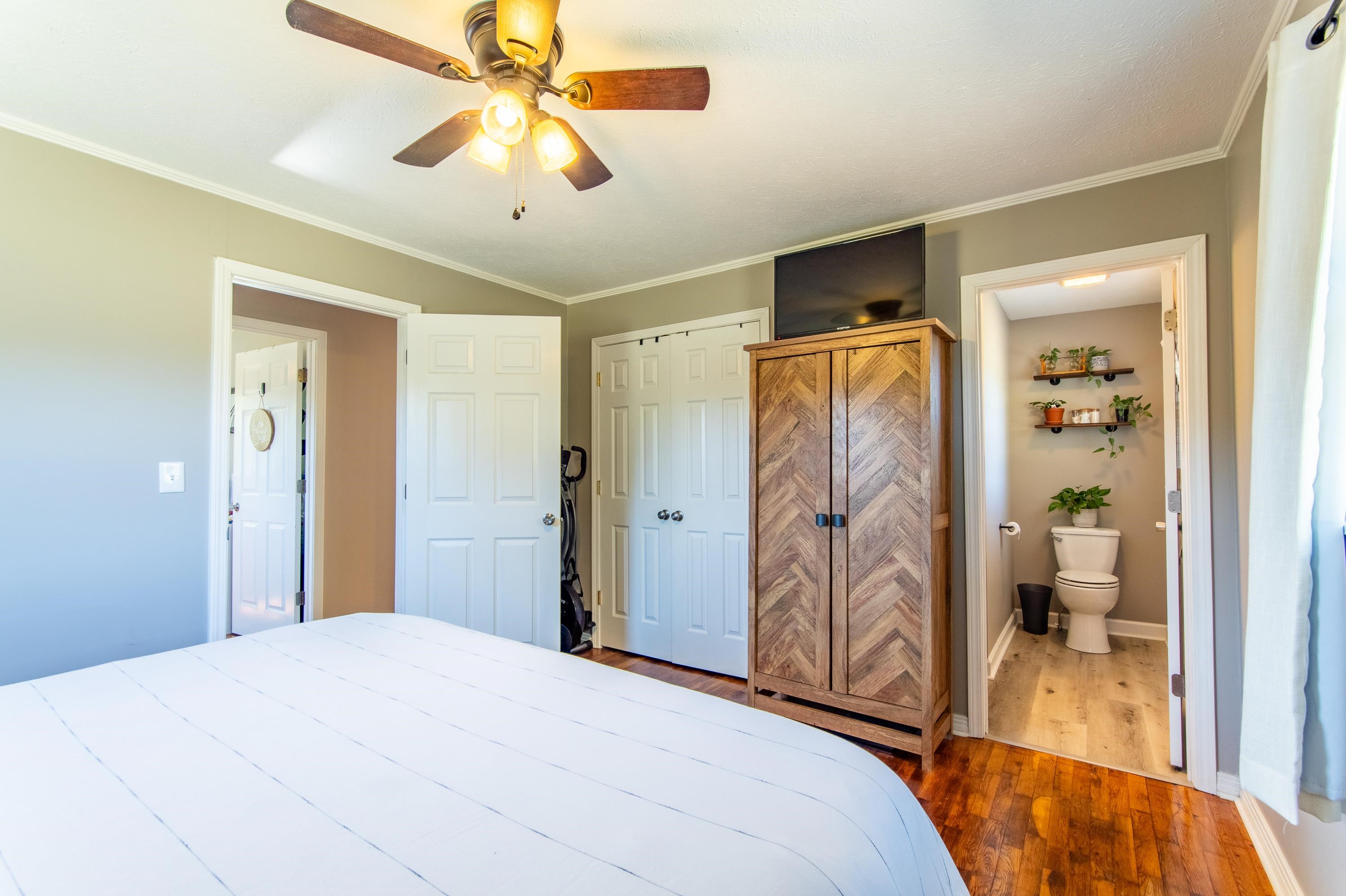 Bedroom featuring dark hardwood / wood-style flooring, ornamental molding, ensuite bath, and ceiling fan