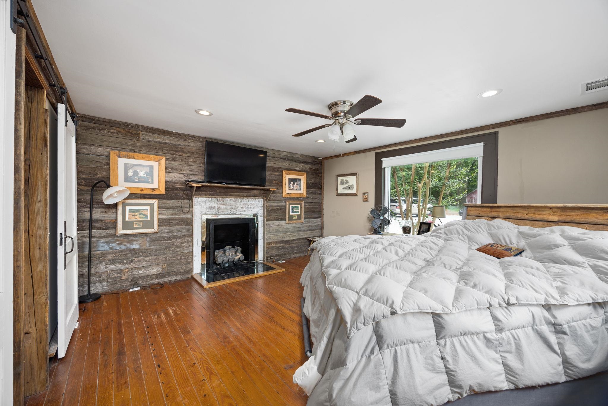 Bedroom featuring hardwood / wood-style floors, wooden walls, crown molding, ceiling fan, and a stone fireplace