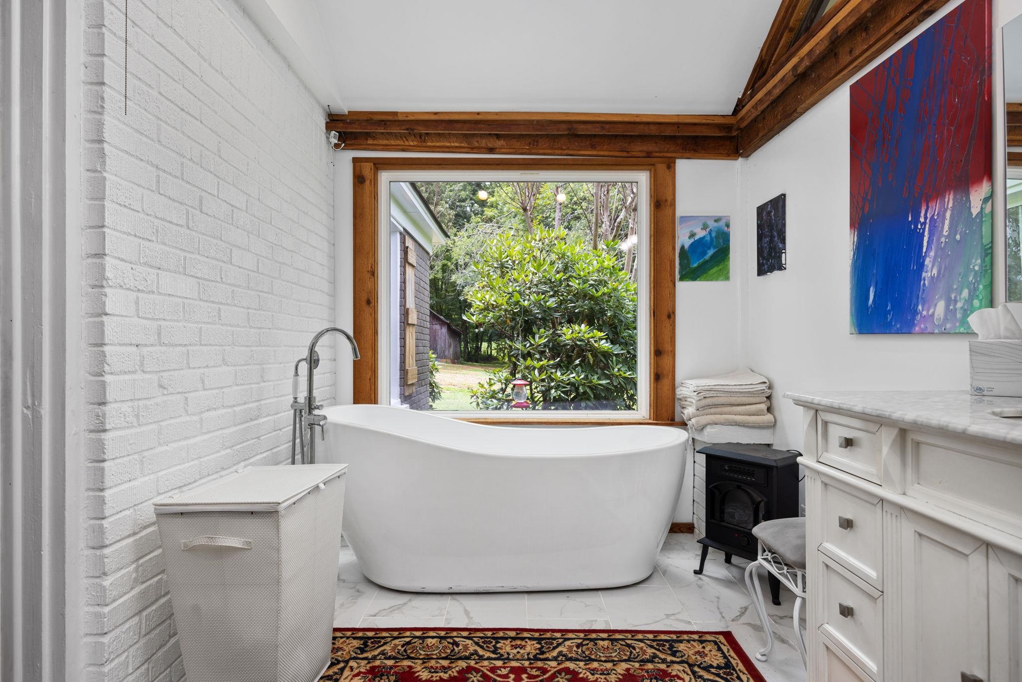 Bathroom featuring a tub, vanity, a wood stove, tile patterned floors, and lofted ceiling