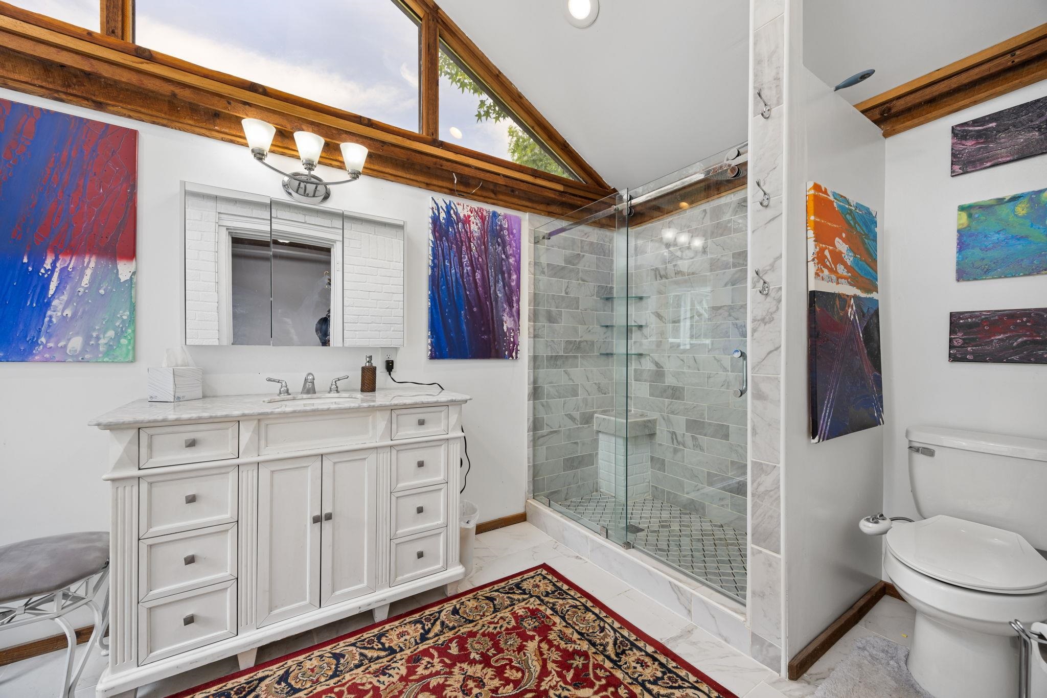 Bathroom featuring tile patterned flooring, vaulted ceiling, walk in shower, toilet, and vanity