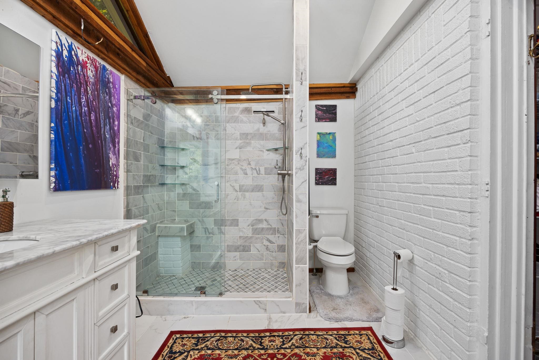 Bathroom with brick wall, vanity, vaulted ceiling, walk in shower, and toilet