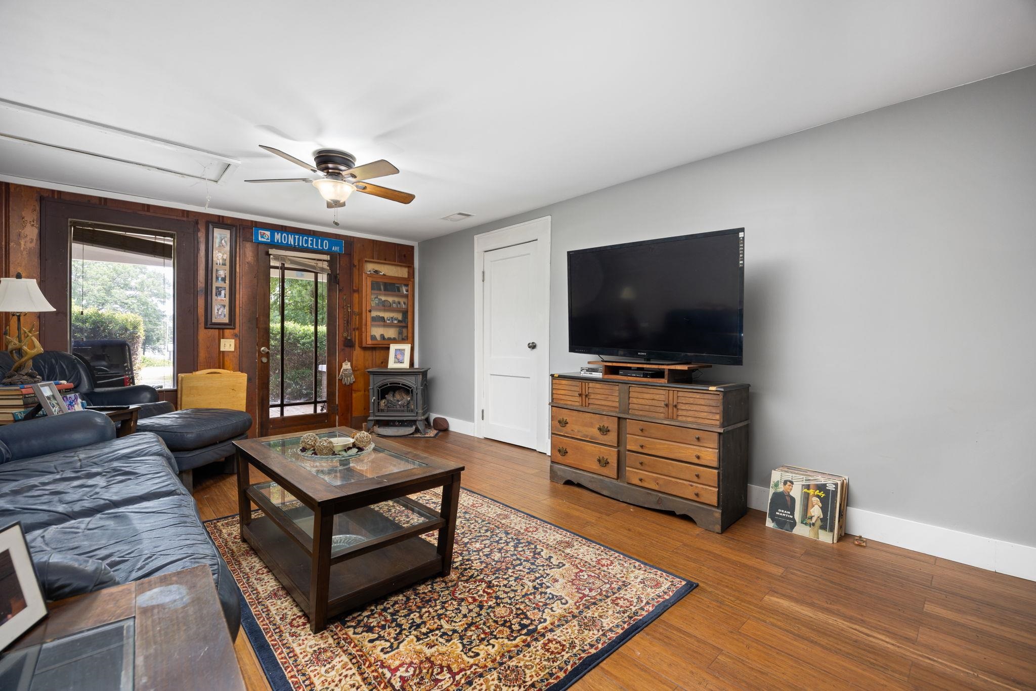 Living room featuring a wood stove, ceiling fan, wood-type flooring, and wooden walls