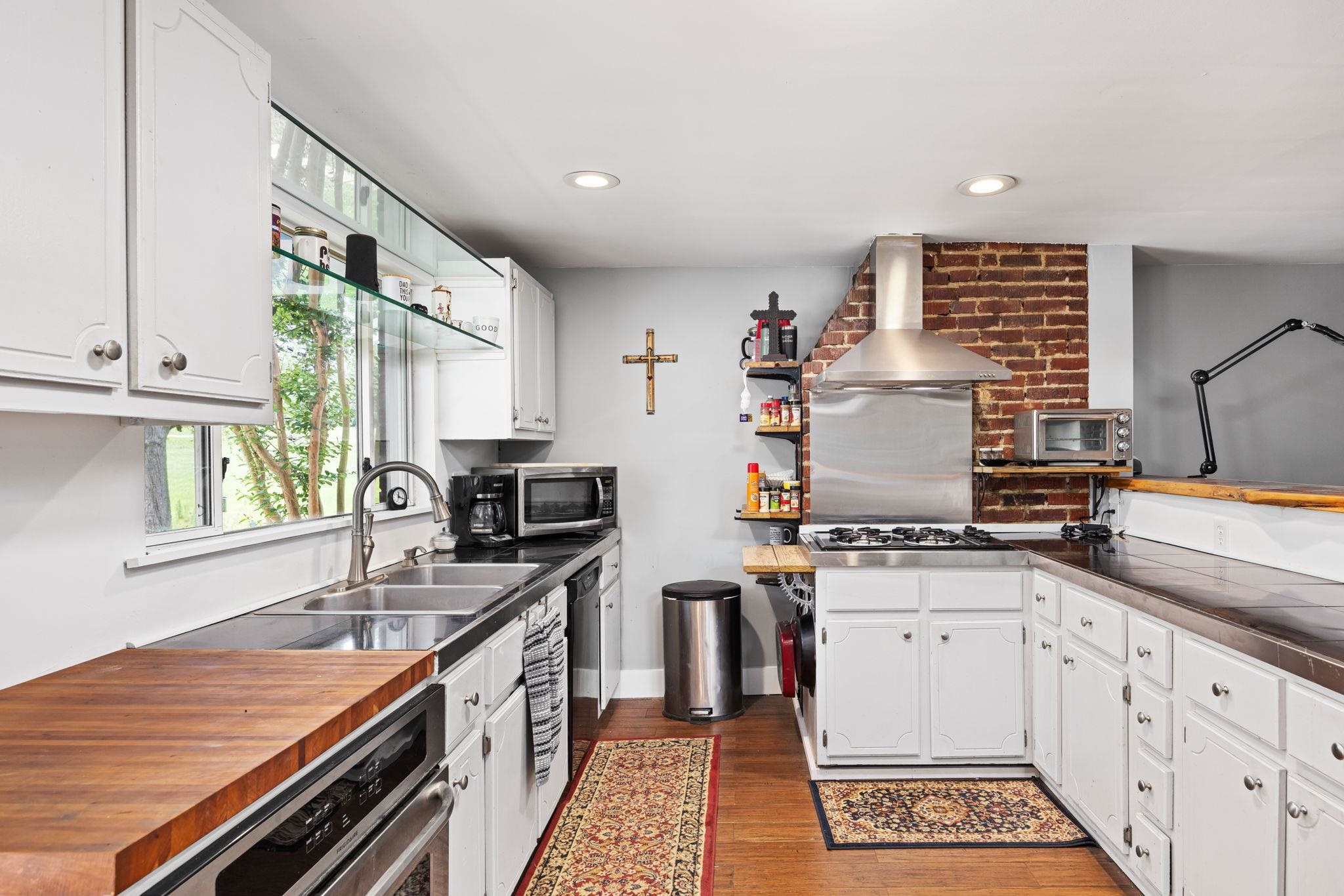 Kitchen with white cabinetry, dark hardwood / wood-style floors, wall chimney exhaust hood, appliances with stainless steel finishes, and brick wall