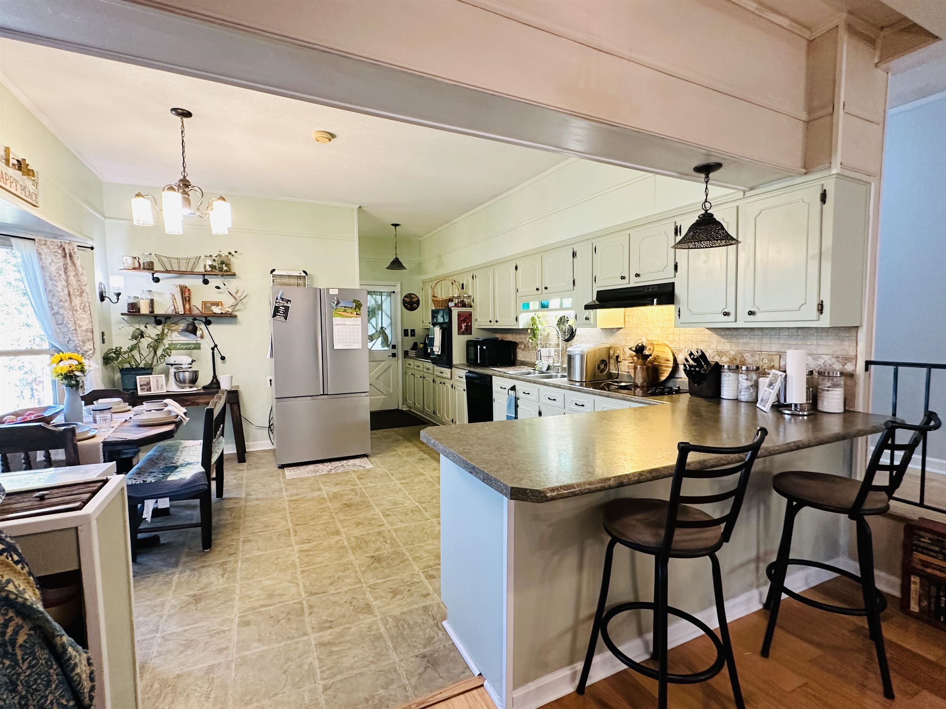 Kitchen featuring an inviting chandelier, stainless steel fridge, light hardwood / wood-style flooring, a breakfast bar, and decorative backsplash