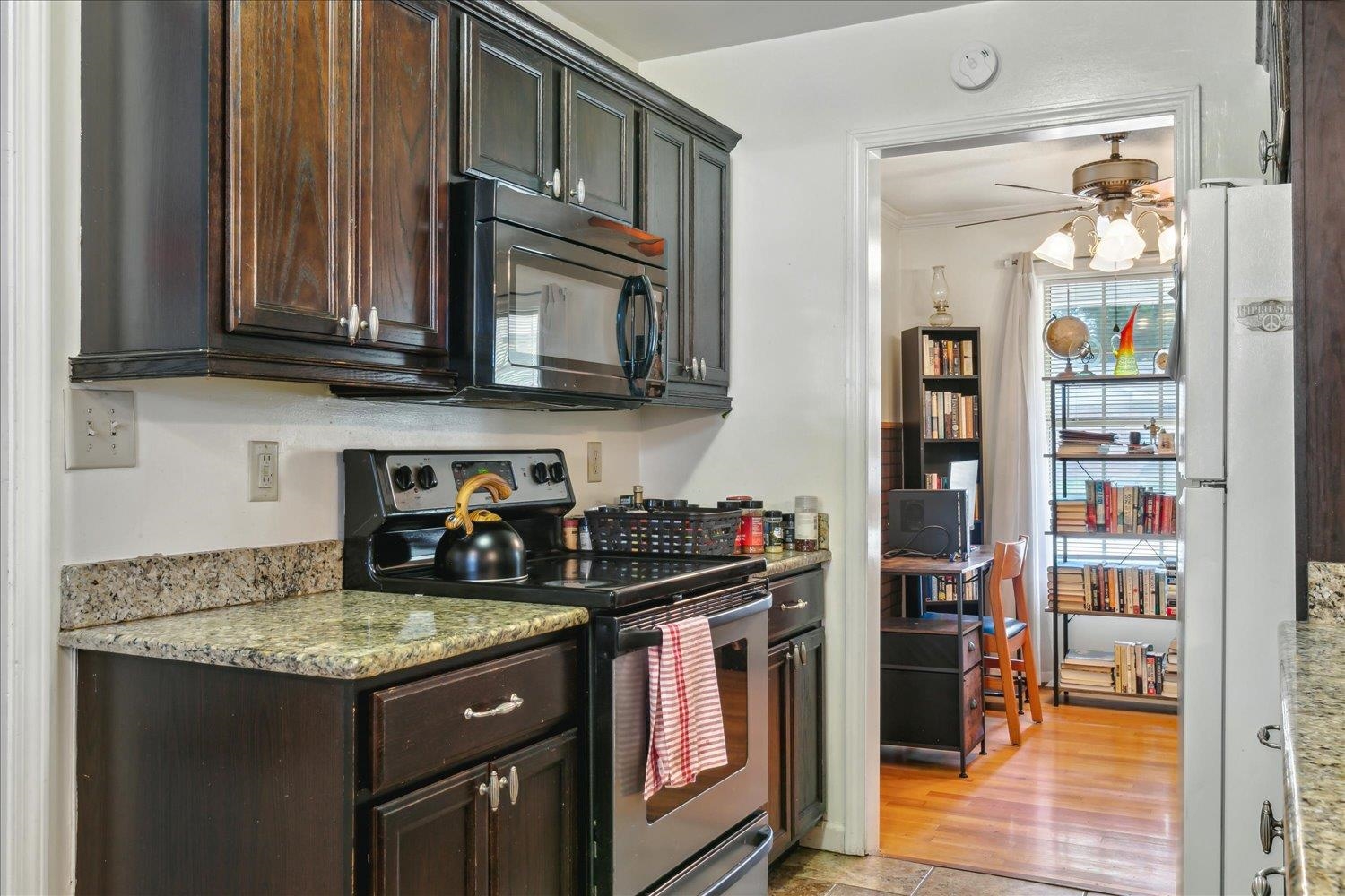 Kitchen with stainless steel electric range, light hardwood / wood-style flooring, light stone counters, ceiling fan, and dark brown cabinetry